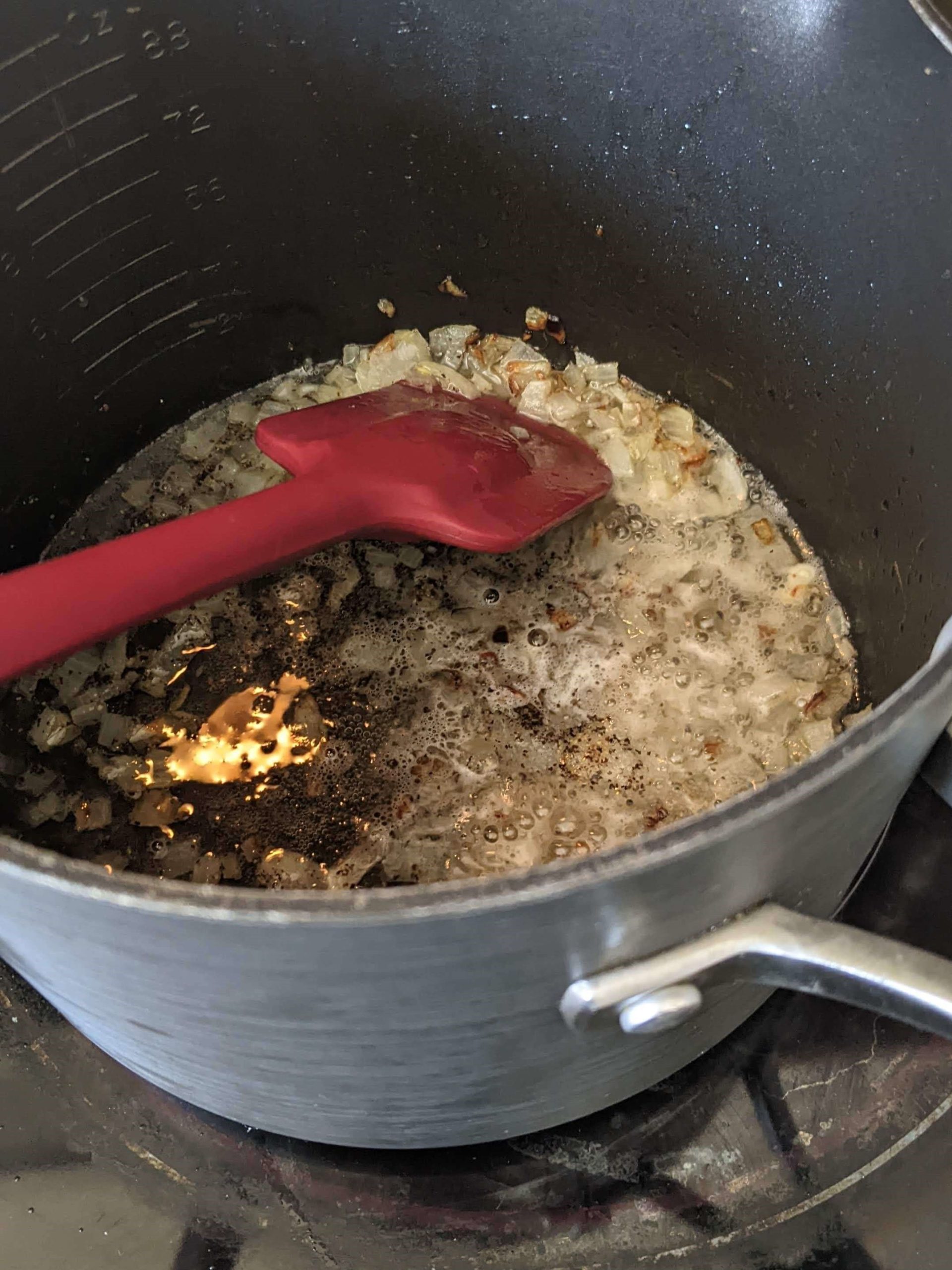 onions sauteing in liquid with a red spatula