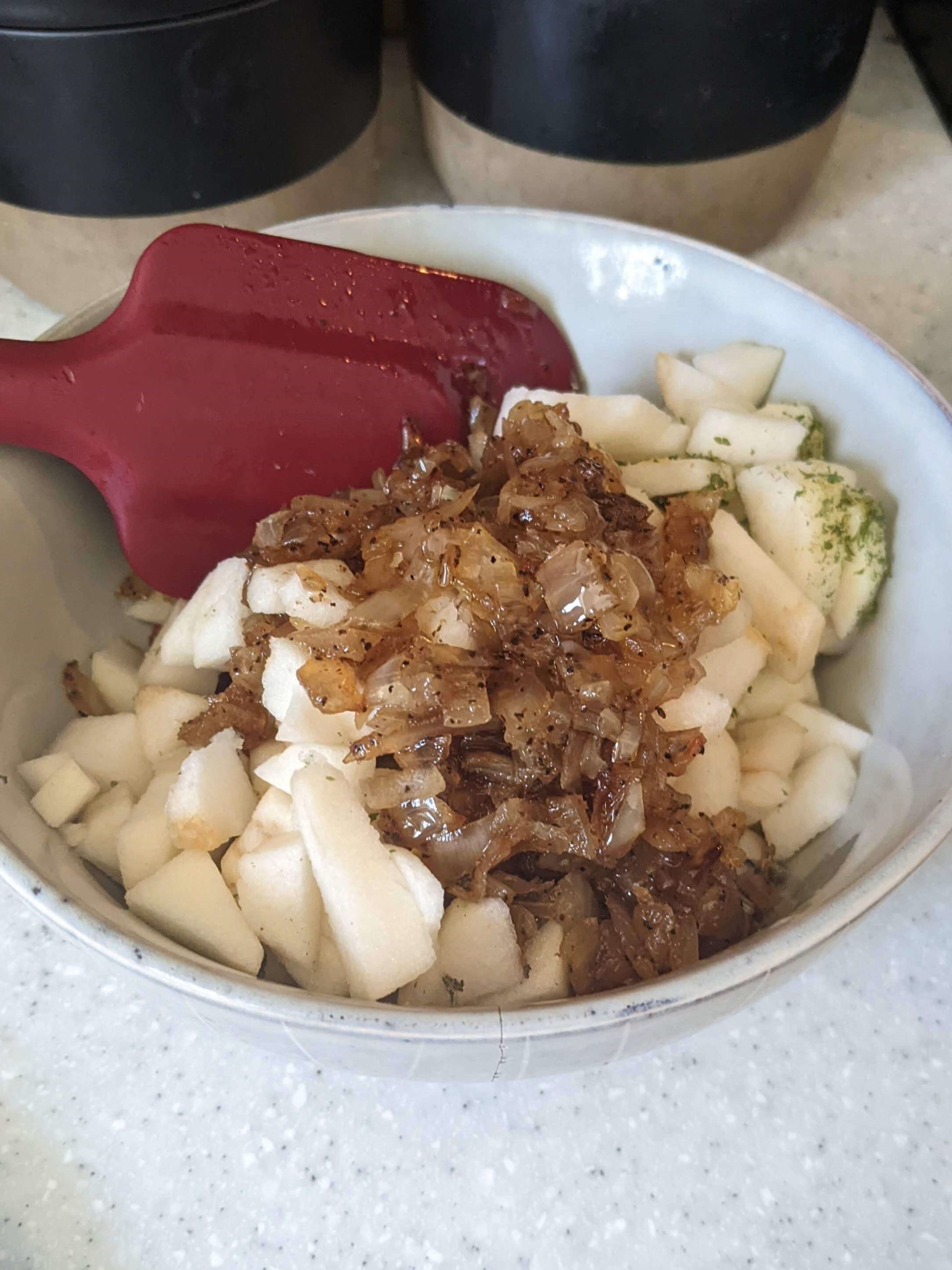 sauteed onions on tops of diced apples in a bowl with a red spatula