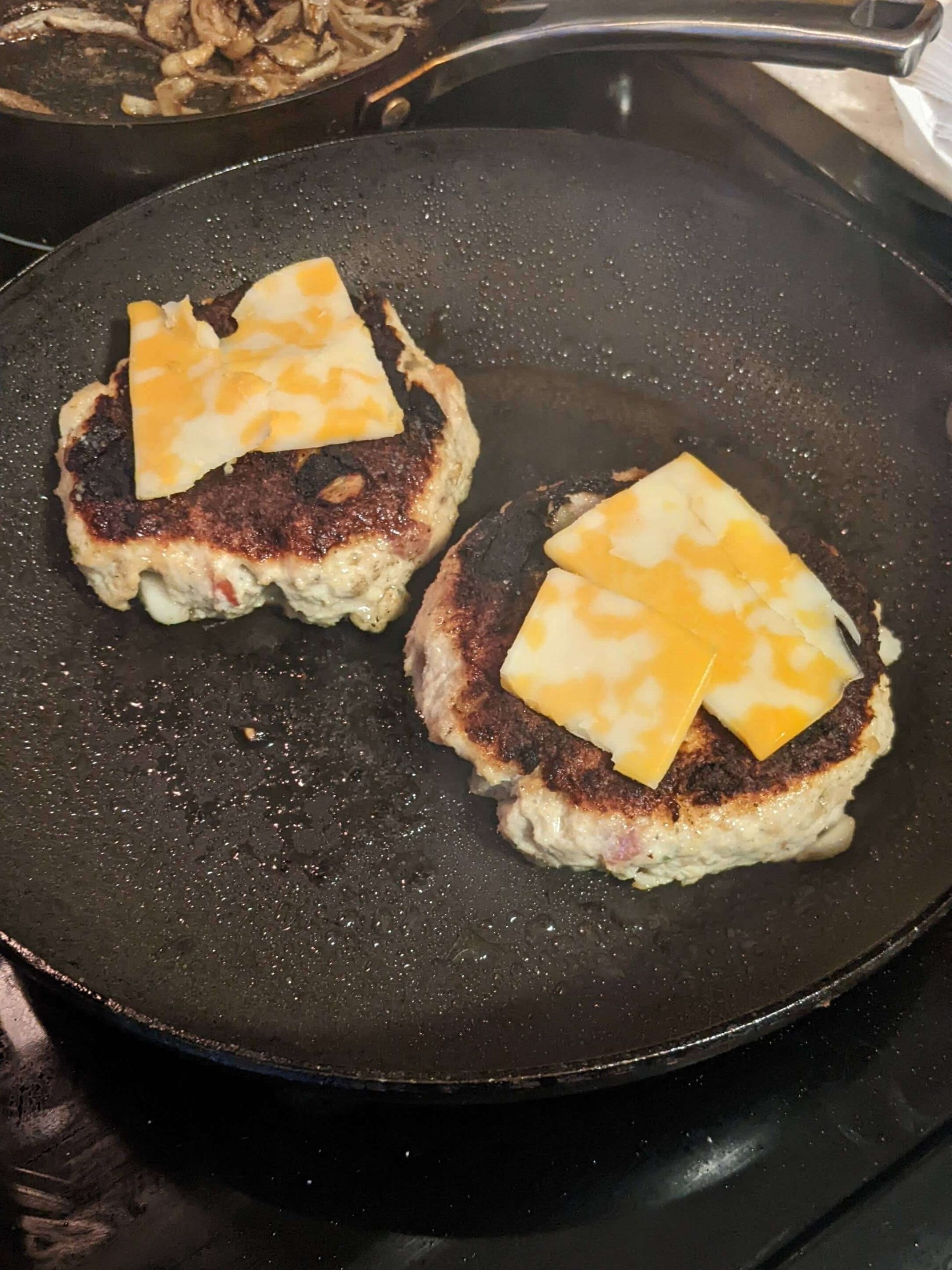 chicken apple burgers with cheese cooking in a pan