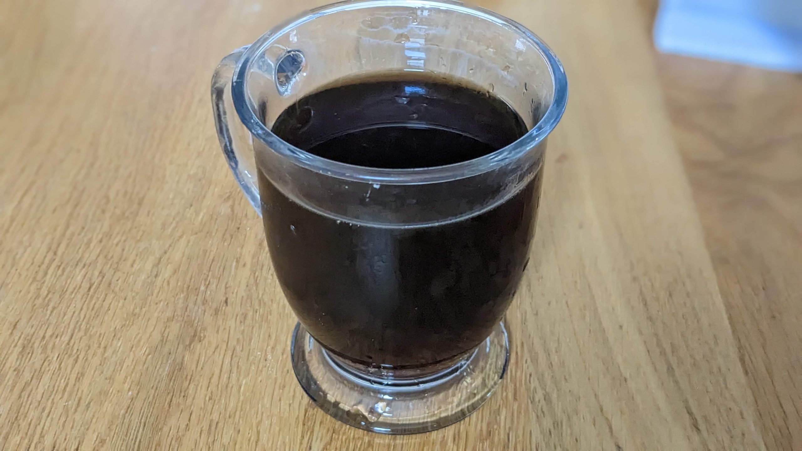 a clear mug with coffee on a wooden counter