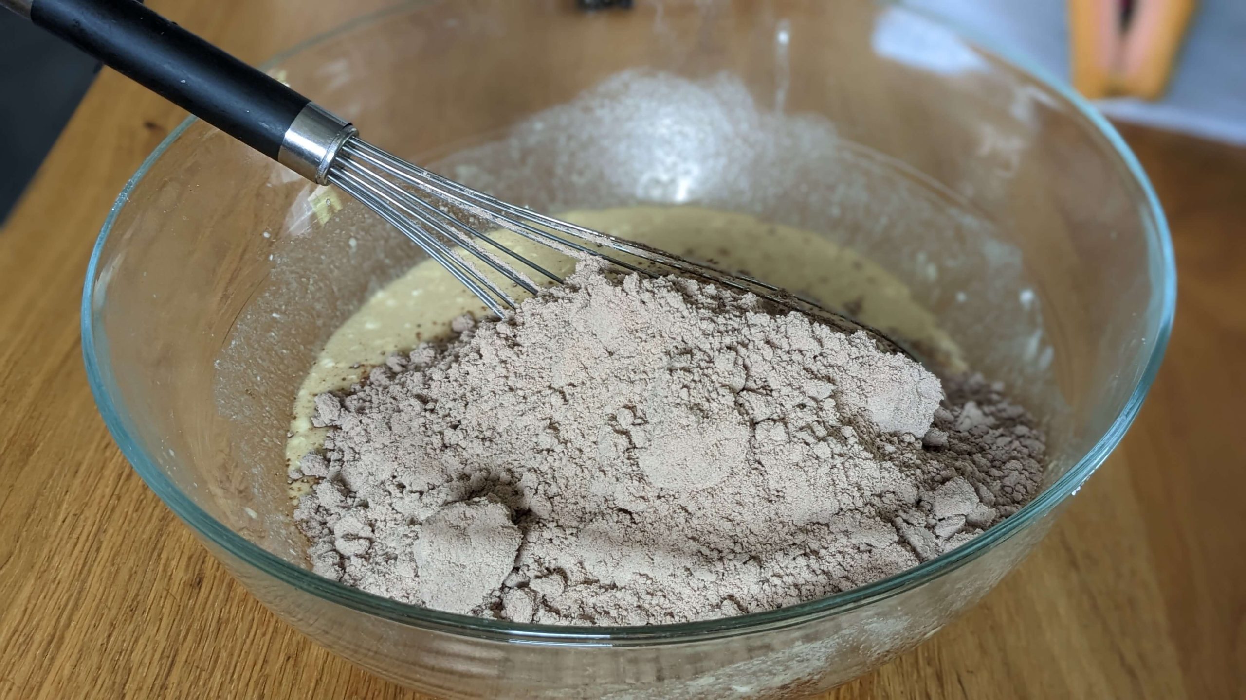 a glass bowl filled with unmixed brownie mix and a whisk