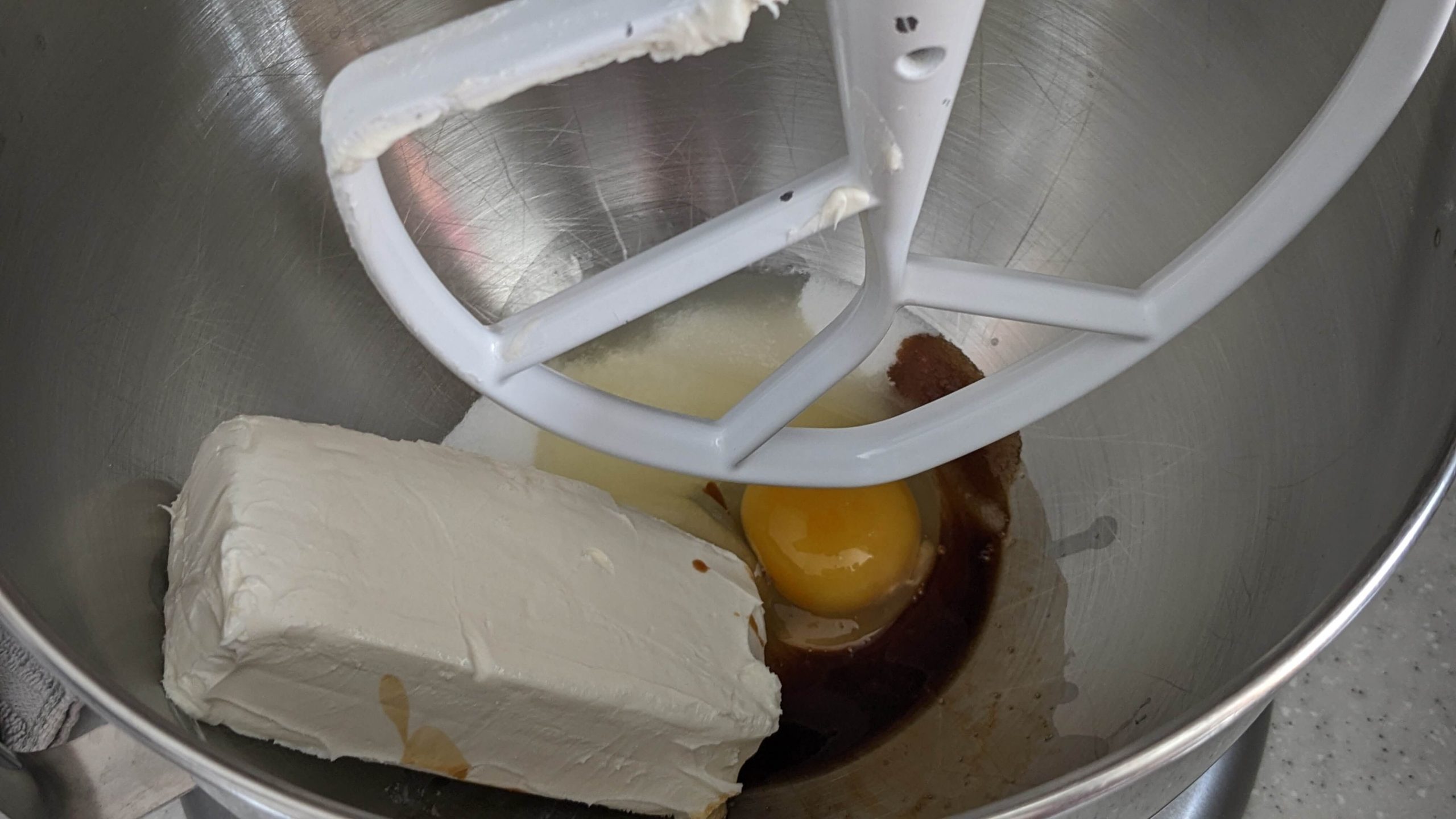 a block of cream cheese and an egg in a silver mixing bowl with a kitchen aid beater attachment