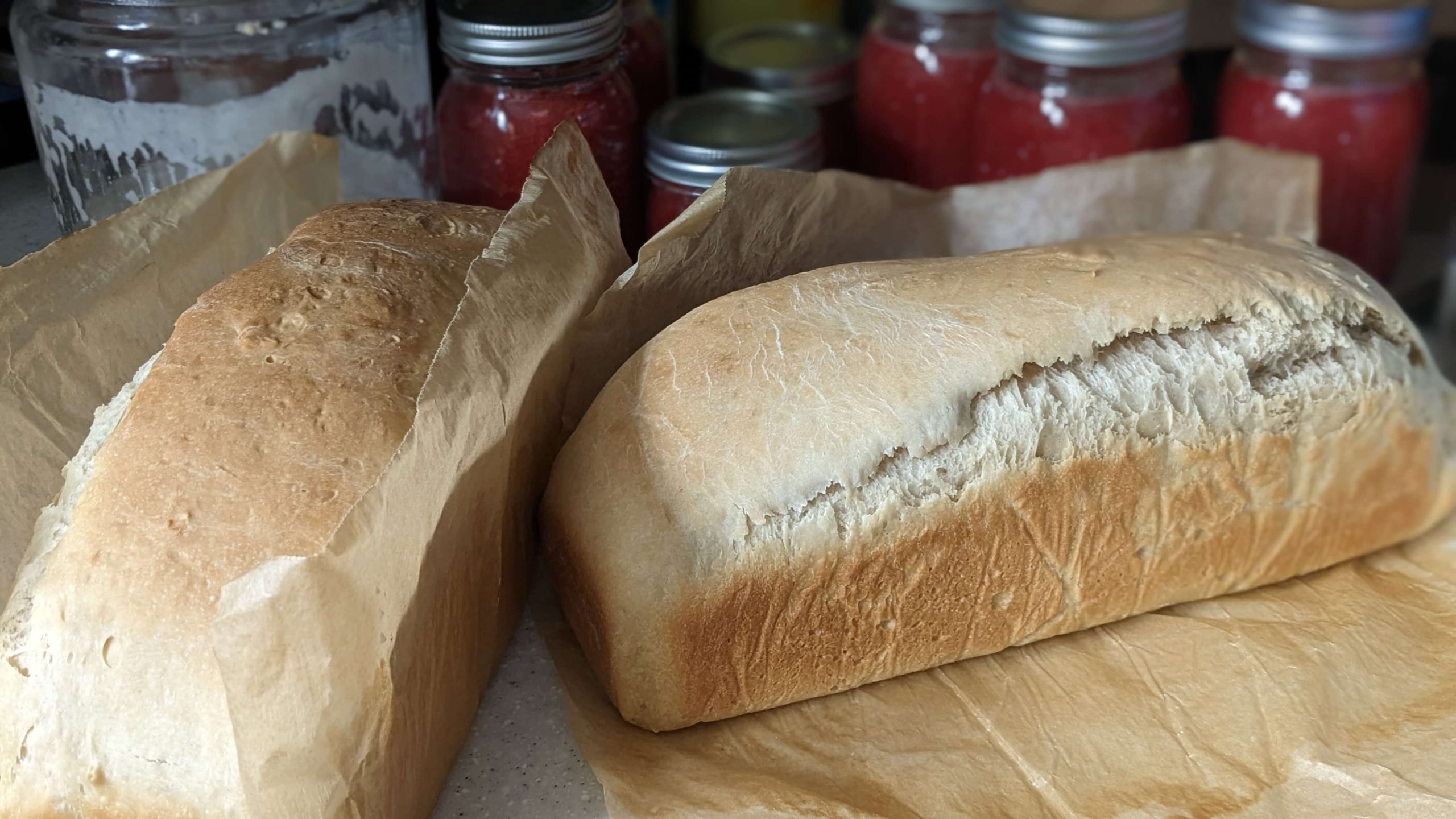 two loaves of sourdough sandwich bread on parchment paper in front of canned jelly