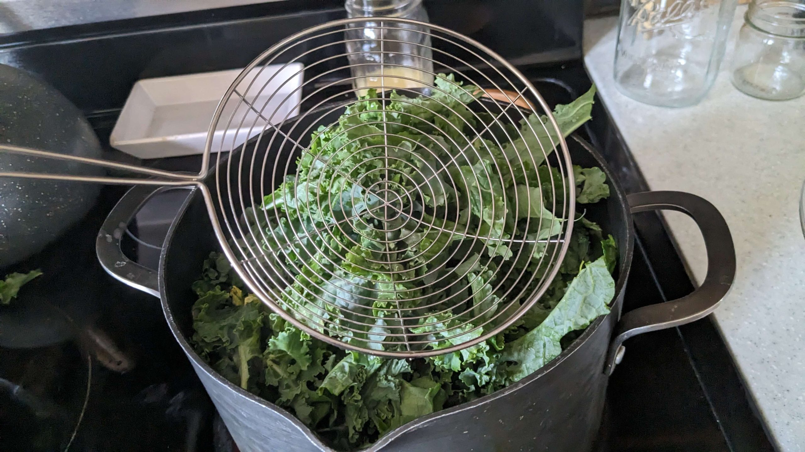 cooking spider on top of kale in a pot of boiling water