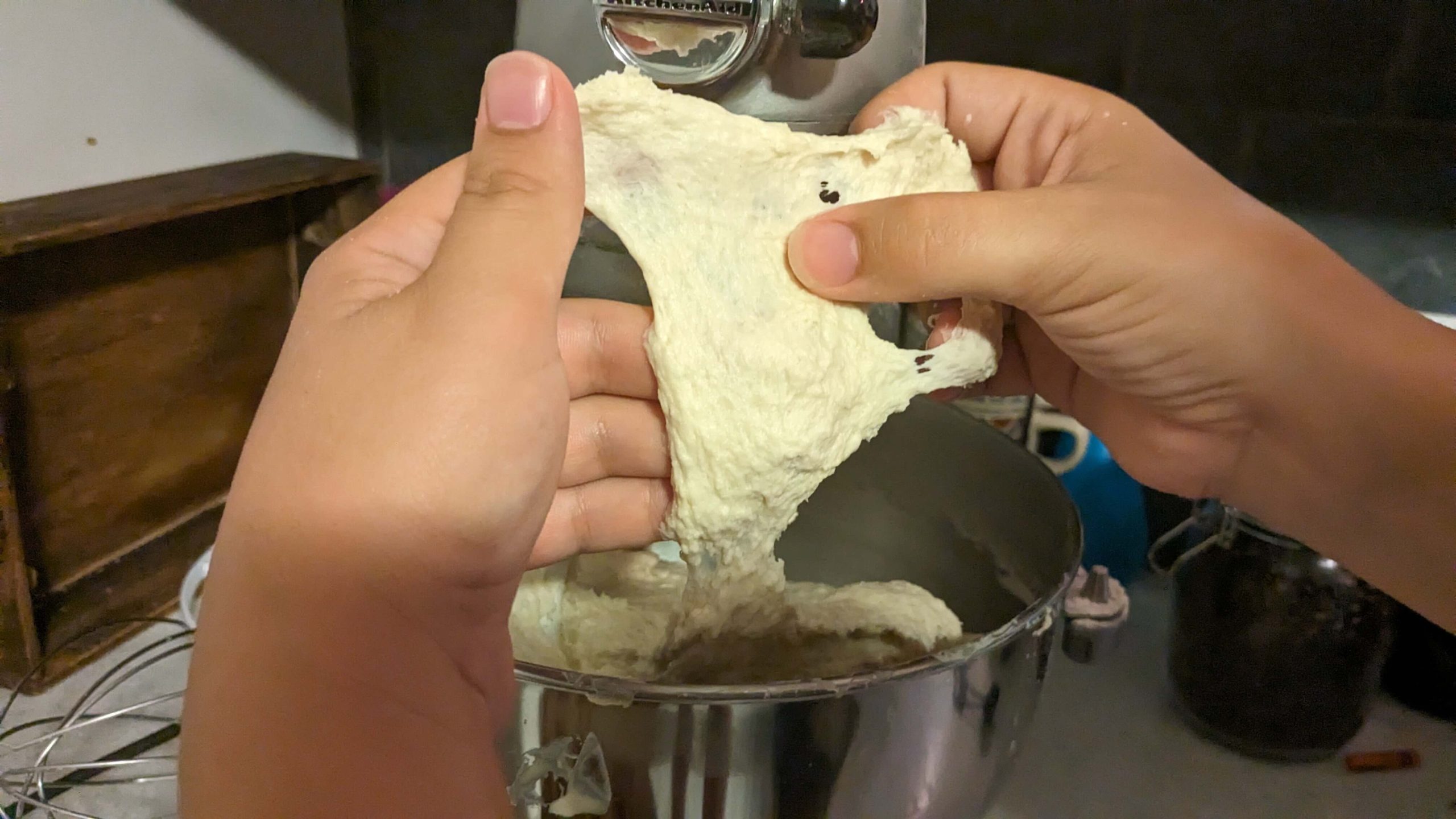 woman stretching dough out of a kitchen aid mixer and pointing at the dough with her thumb