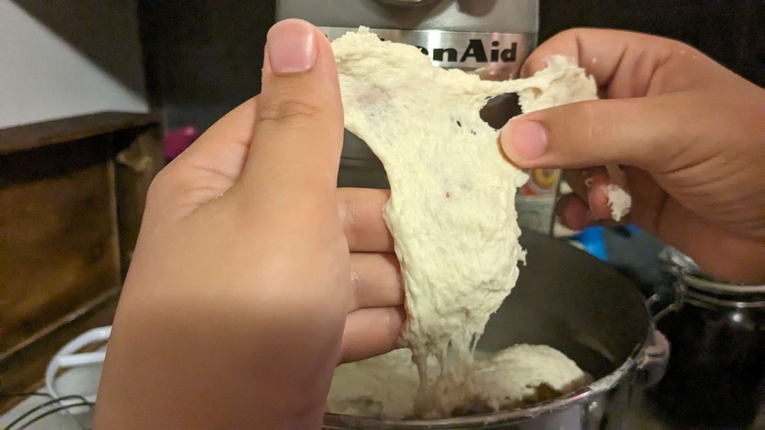 woman stretching dough out of a kitchen aid mixer and pointing at the dough with her thumb ripping one section