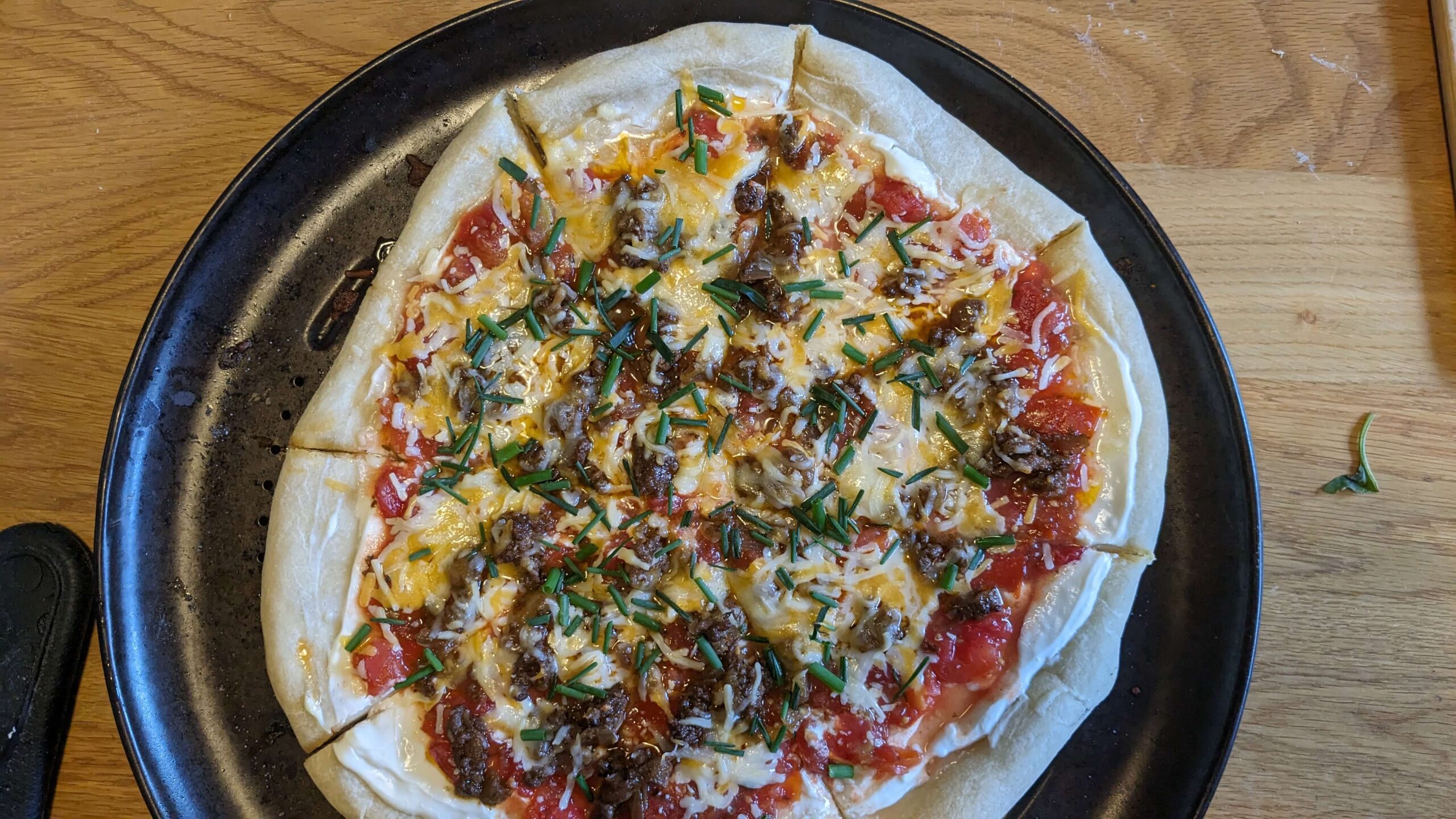 cooked and sliced taco pizza topped with chopped chives