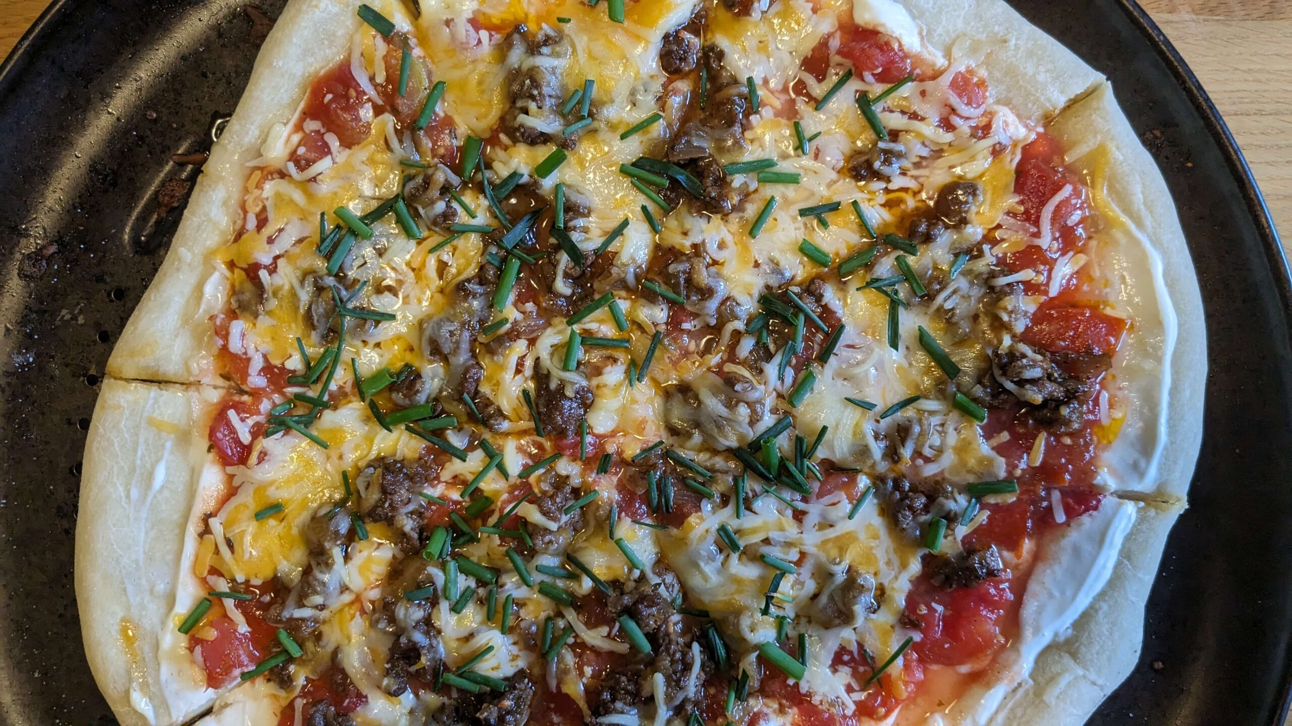 sliced cooked taco pizza topped with chopped green chives 