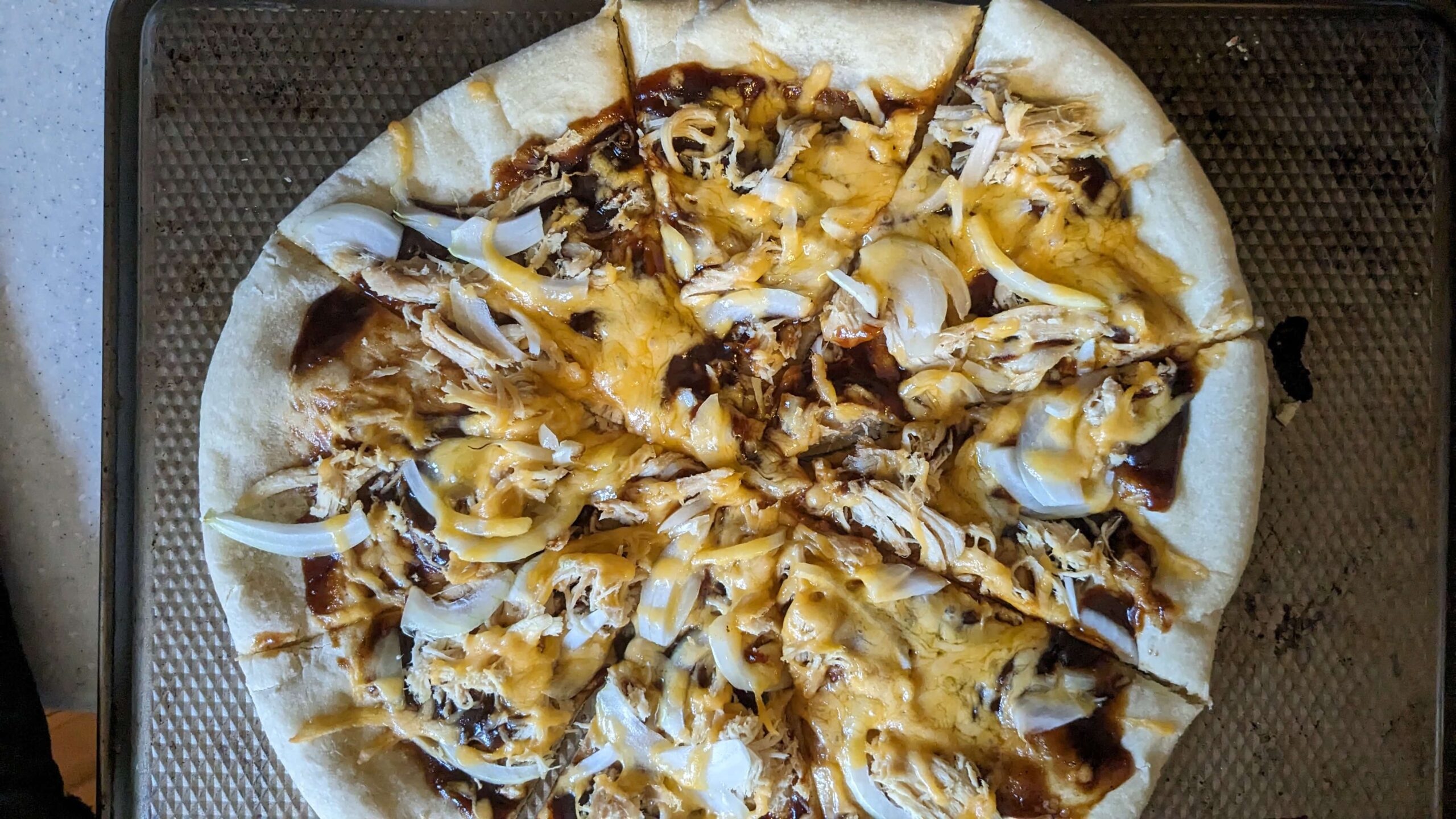 cooked and sliced barbecue chicken pizza with cheddar cheese and onions