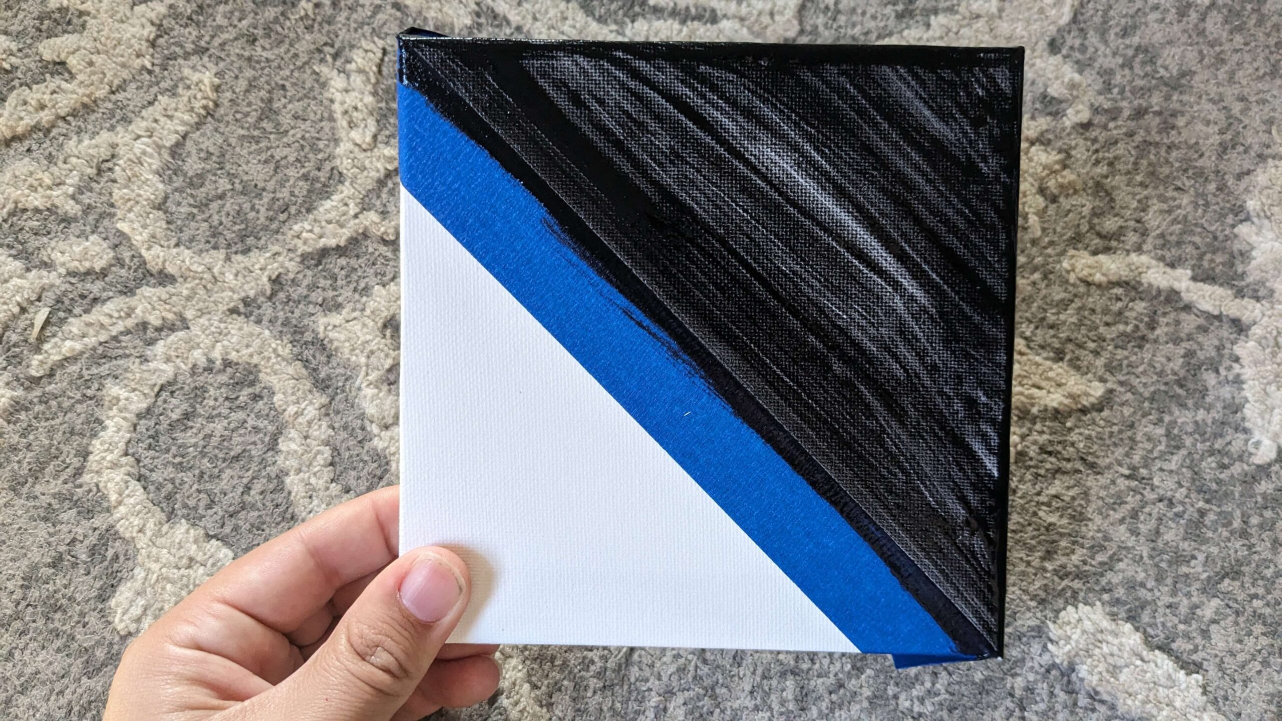 woman holding a square canvas with a diagonal blue painters tape strip and one half painted black