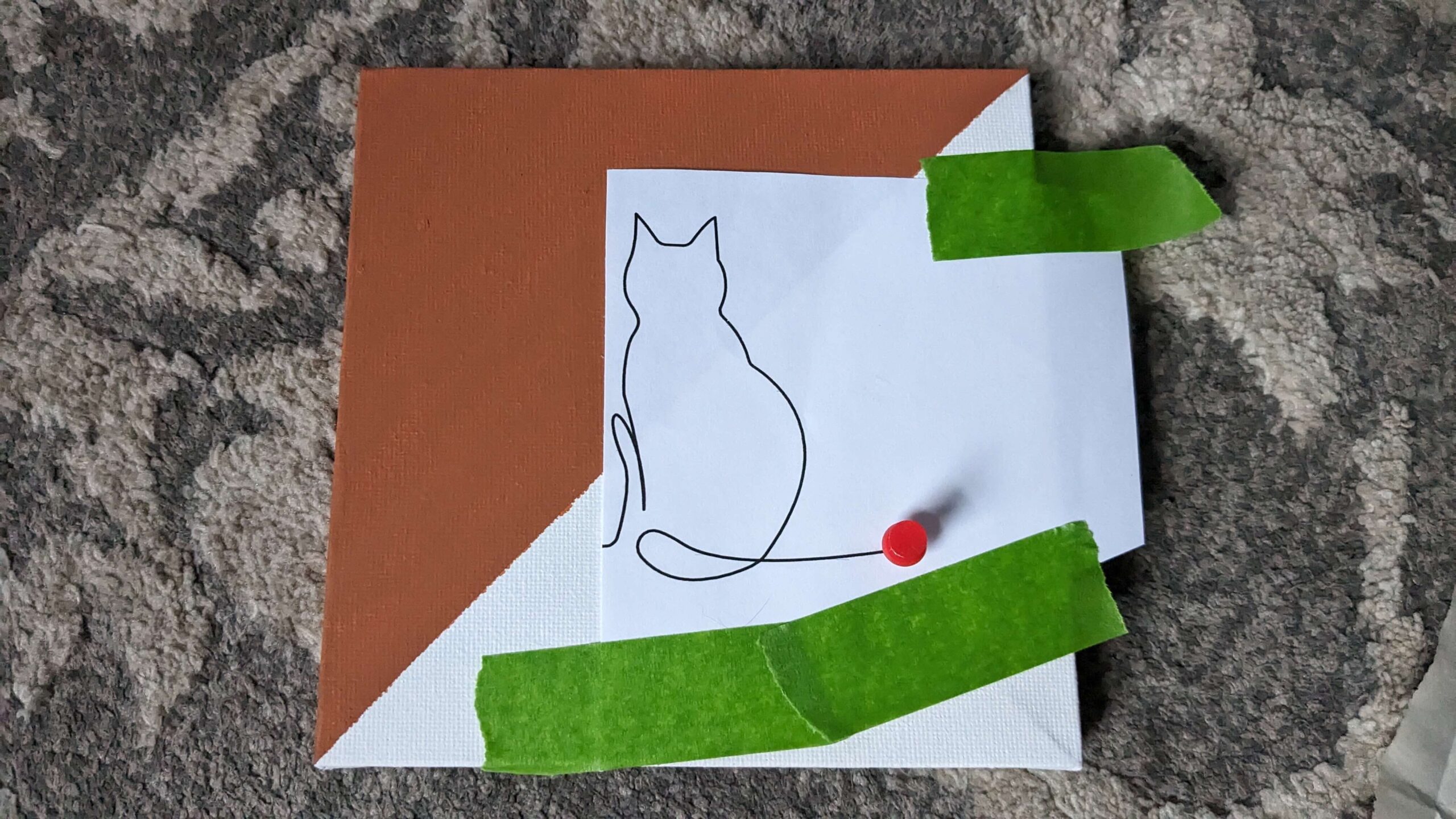 Orange and white square canvas with a cat line art picture taped to it with green painters tape and a red thumbtack