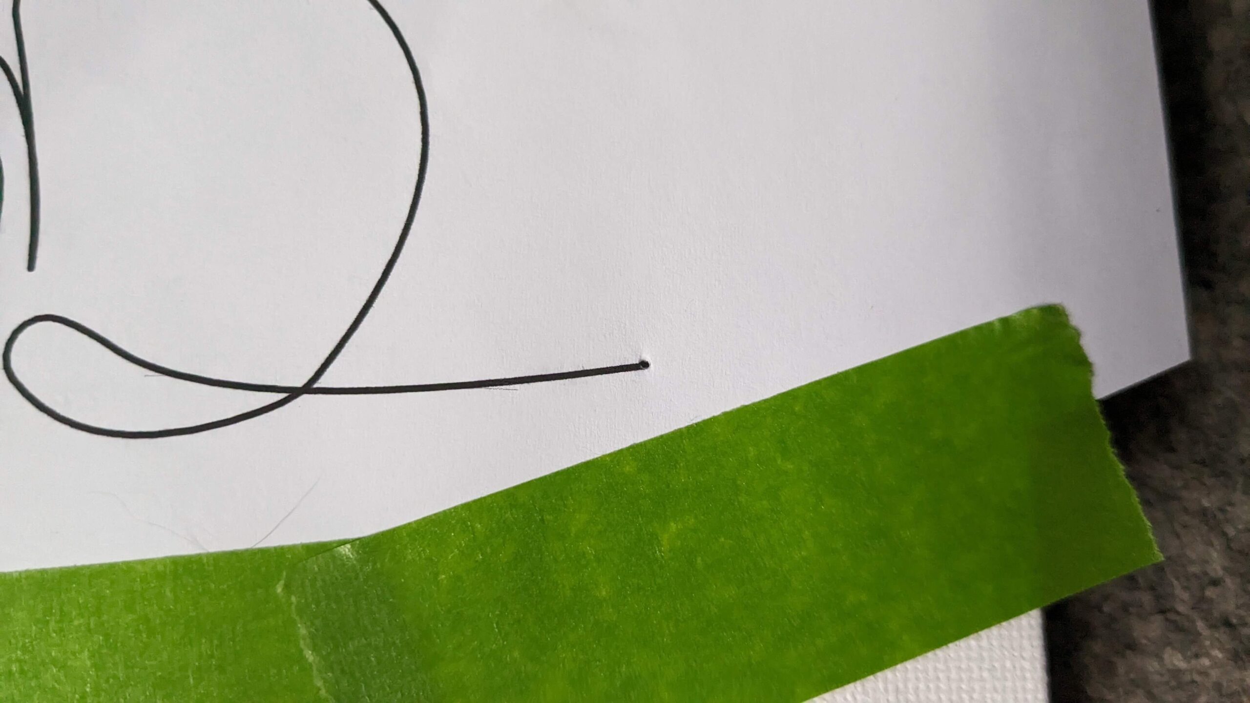 close up of a line on paper with a small hole and green painters tape