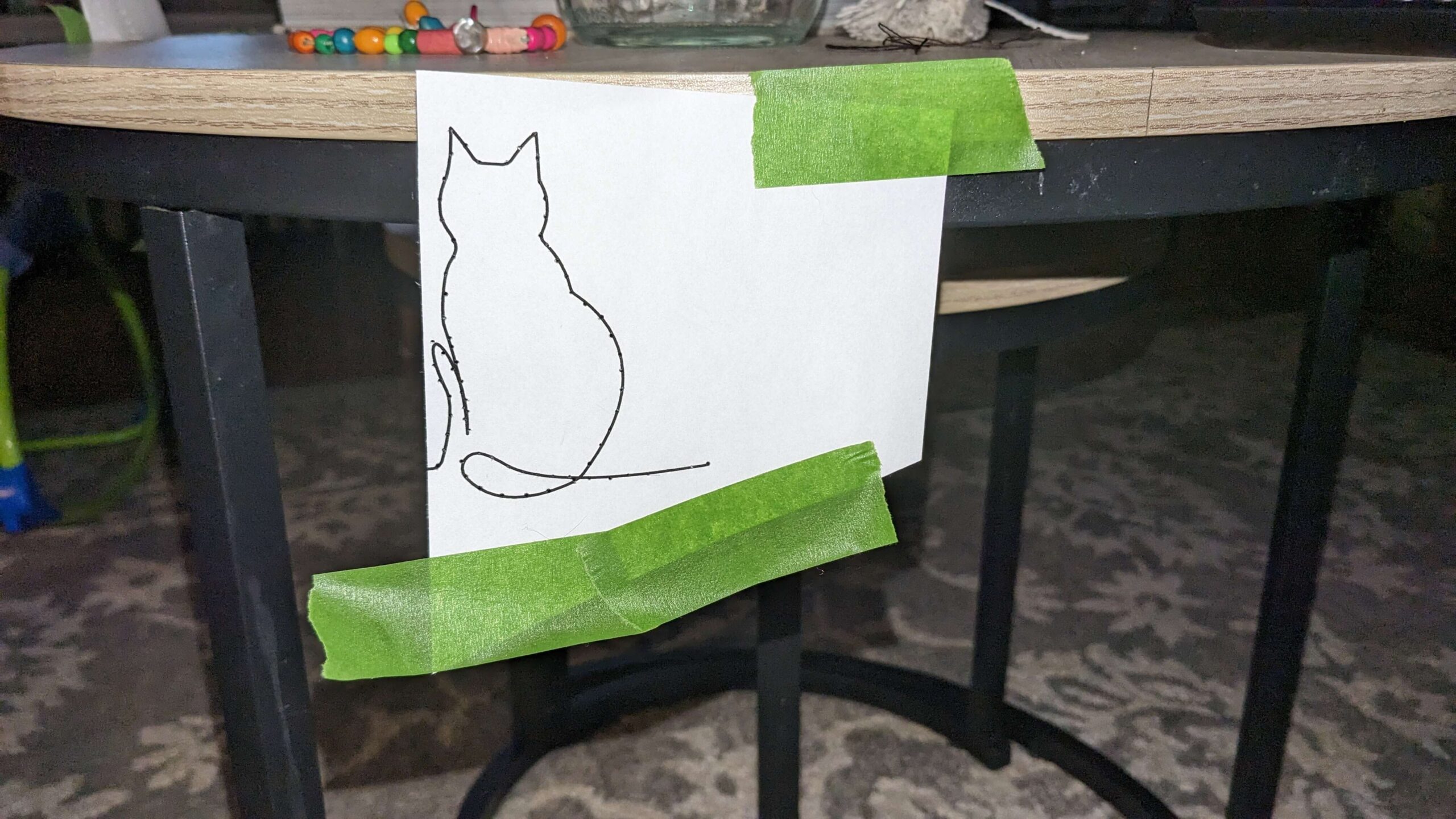 cat line art picture taped to a table with green painters tape with small holes