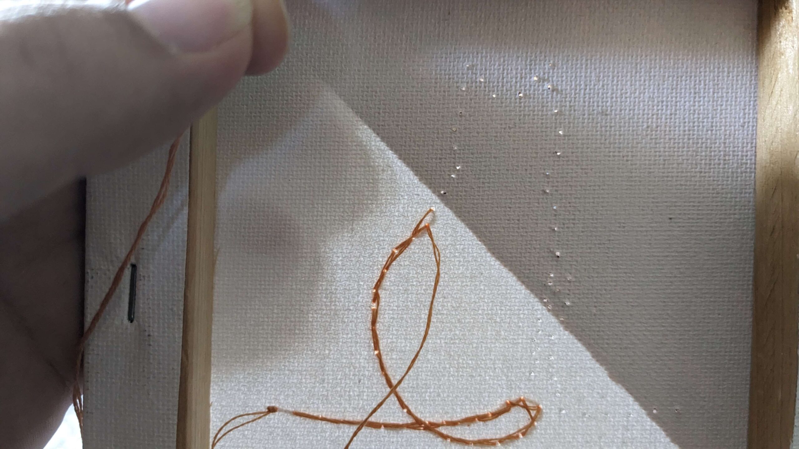 back of a canvas with orange embroidery floss