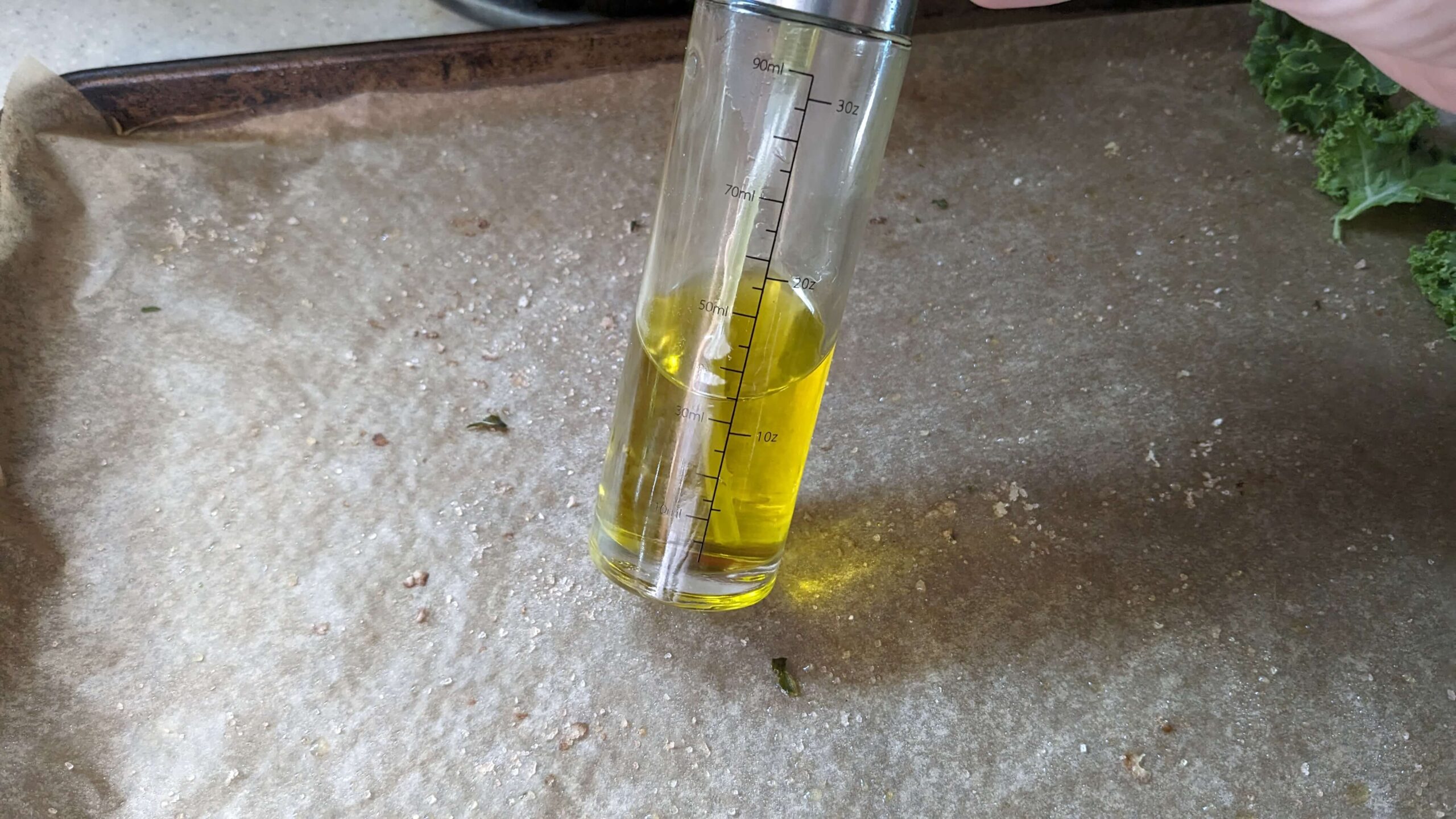spray bottle of olive oil leaning on parchment paper