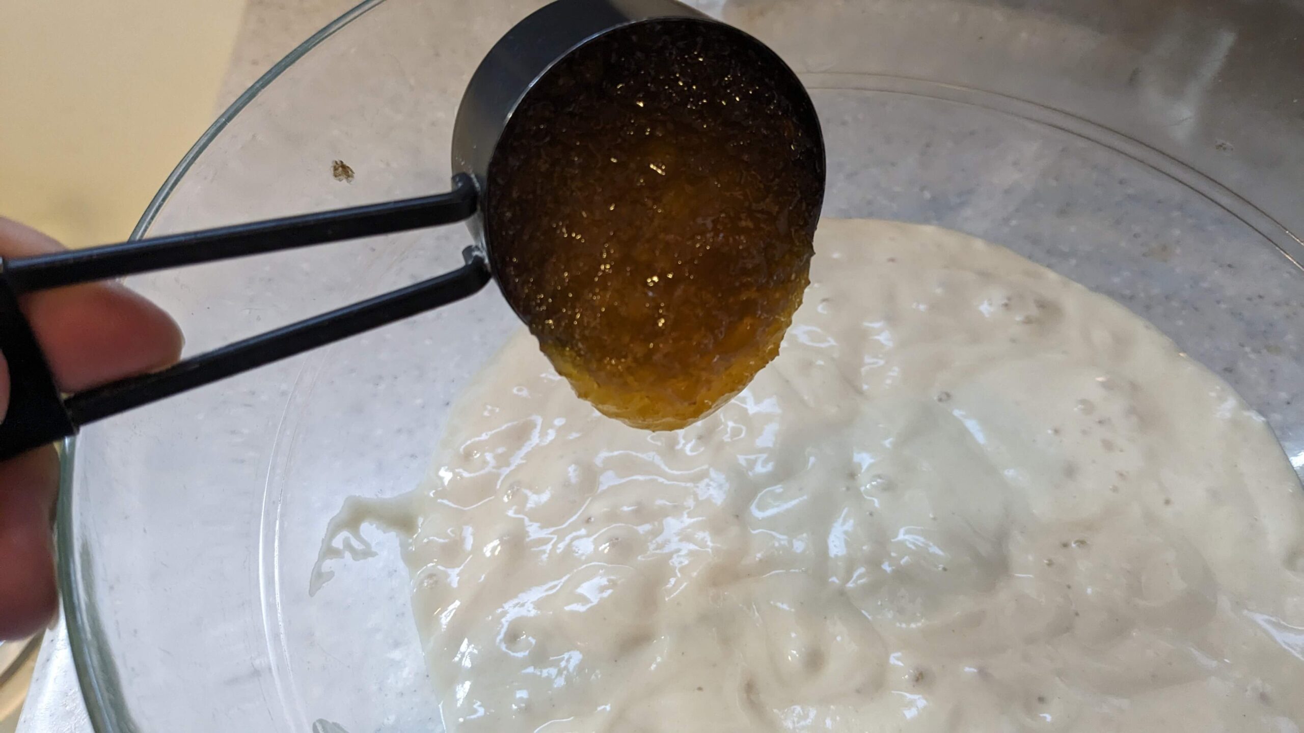 measuring cup pouring honey into a bowl of sourdough discard