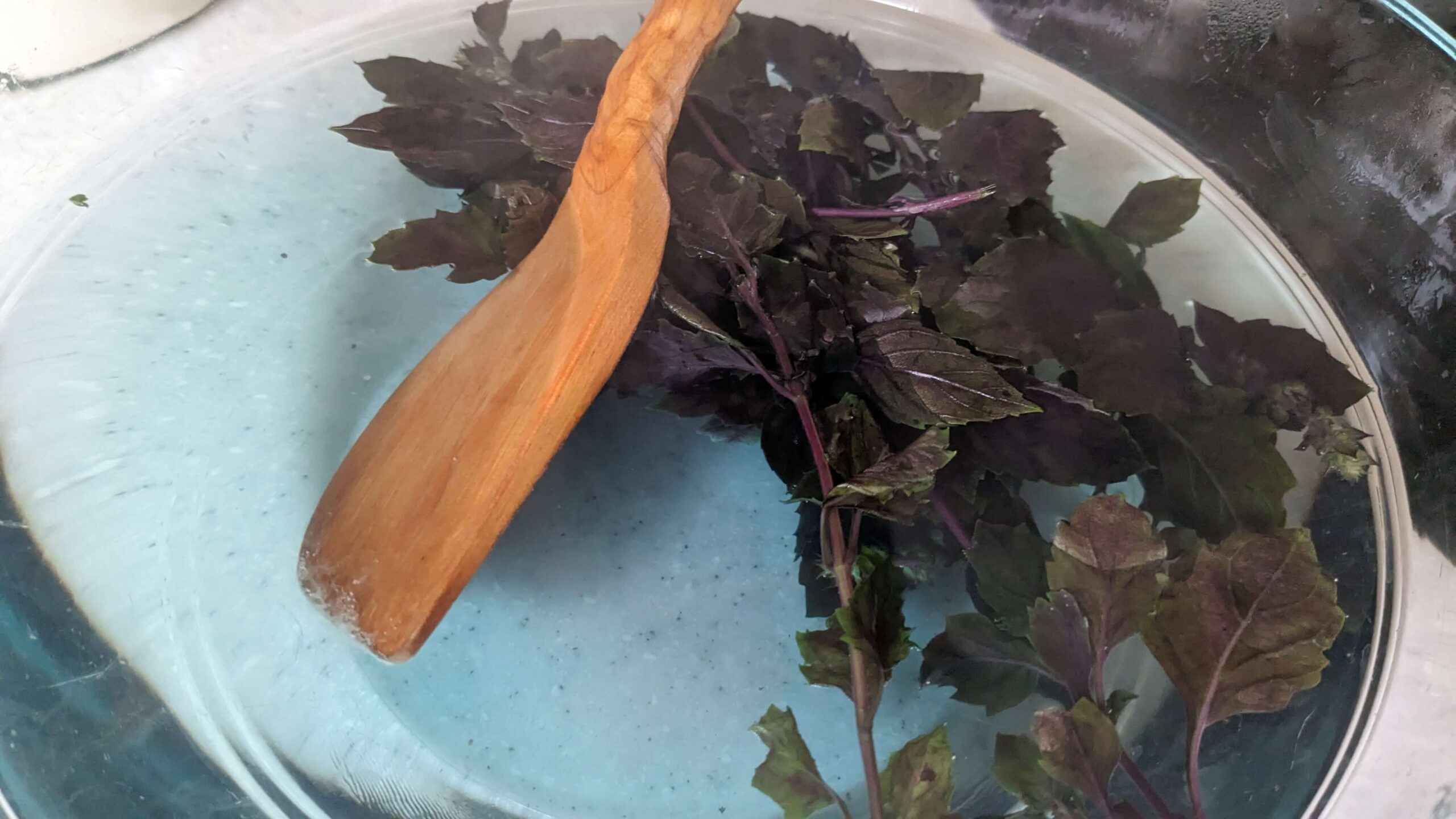 stirring basil leaves with a wooden spatula in a bowl of water that is turning blue