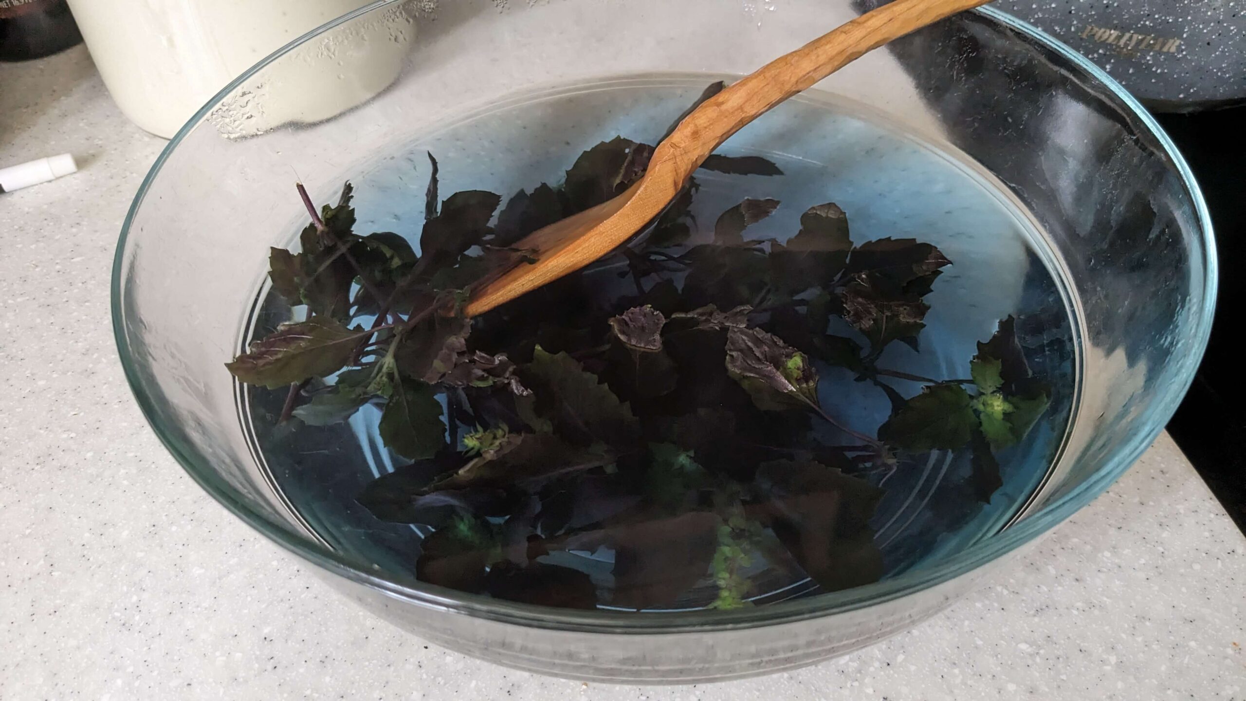 stirring basil leaves with a wooden spatula in a bowl of blue water