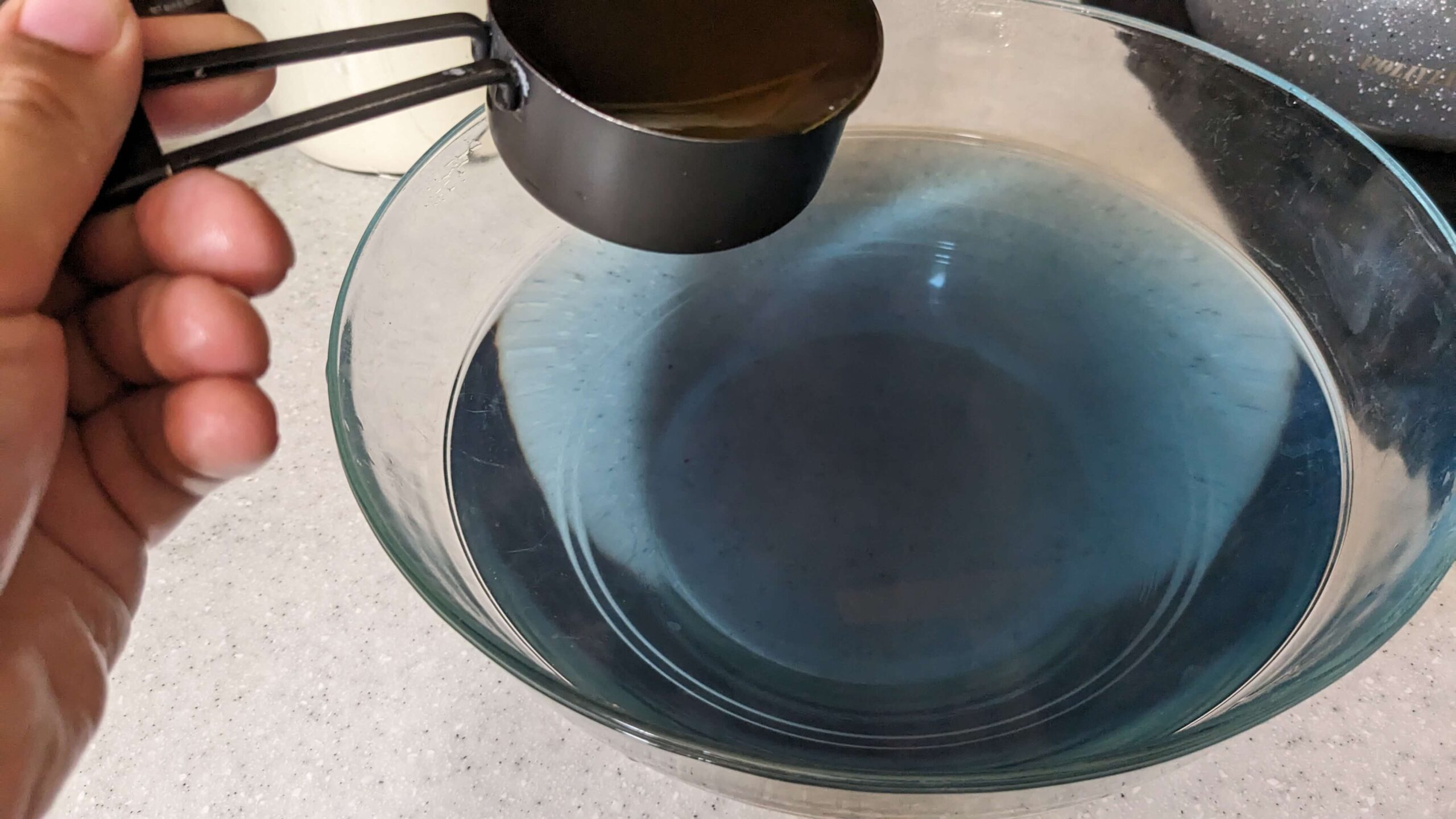 woman holding a measuring cup above a bowl of blue liquid