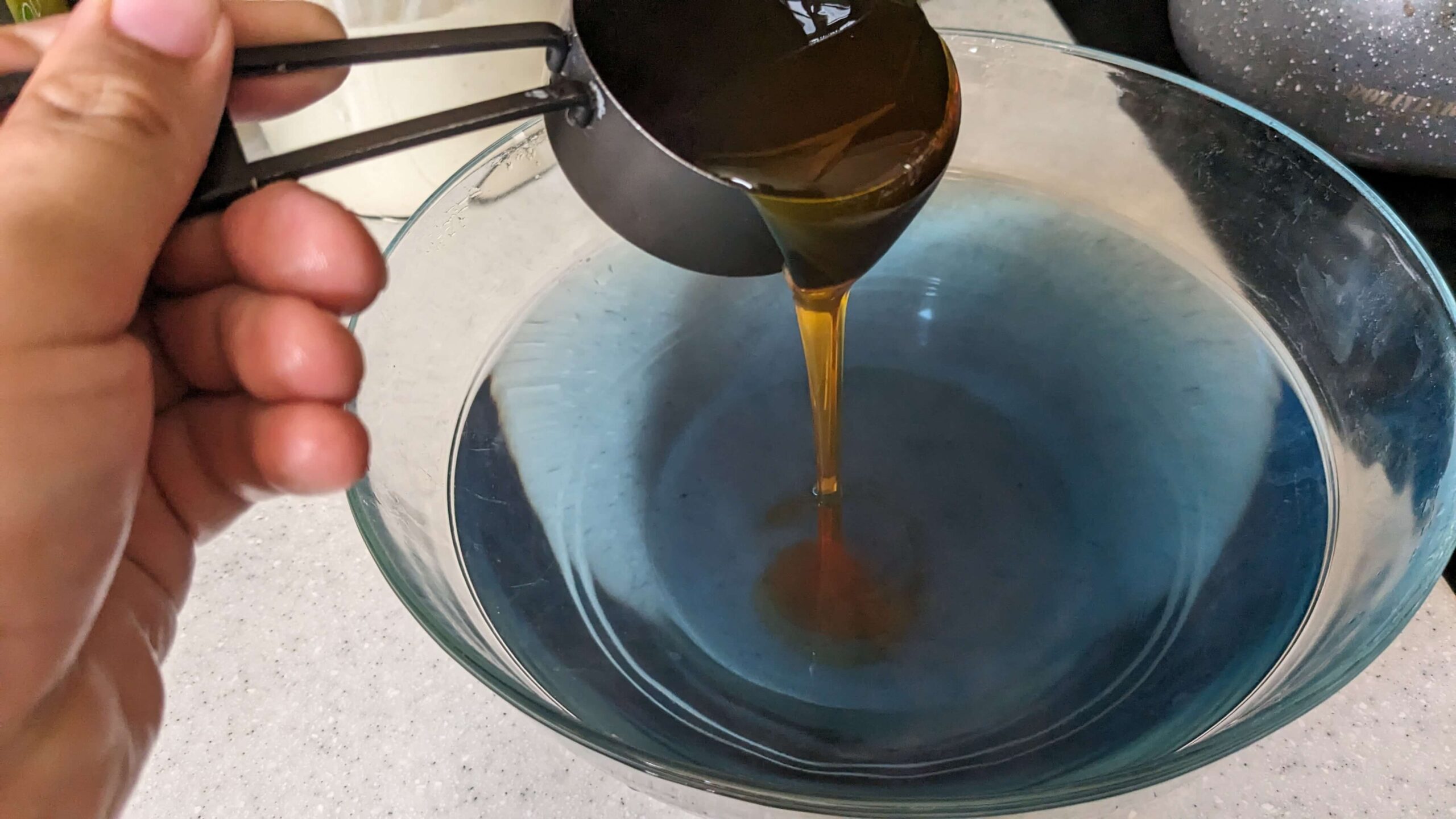 woman pouring honey out of a measuring cup into a bowl of blue liquid