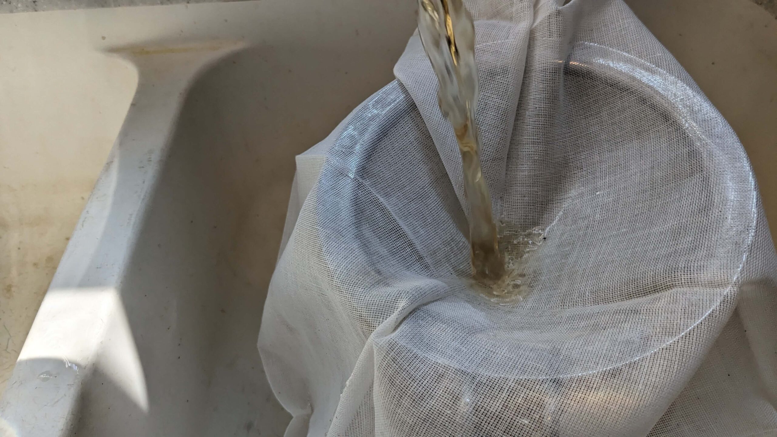 basil tea pouring into cheesecloth in a strainer