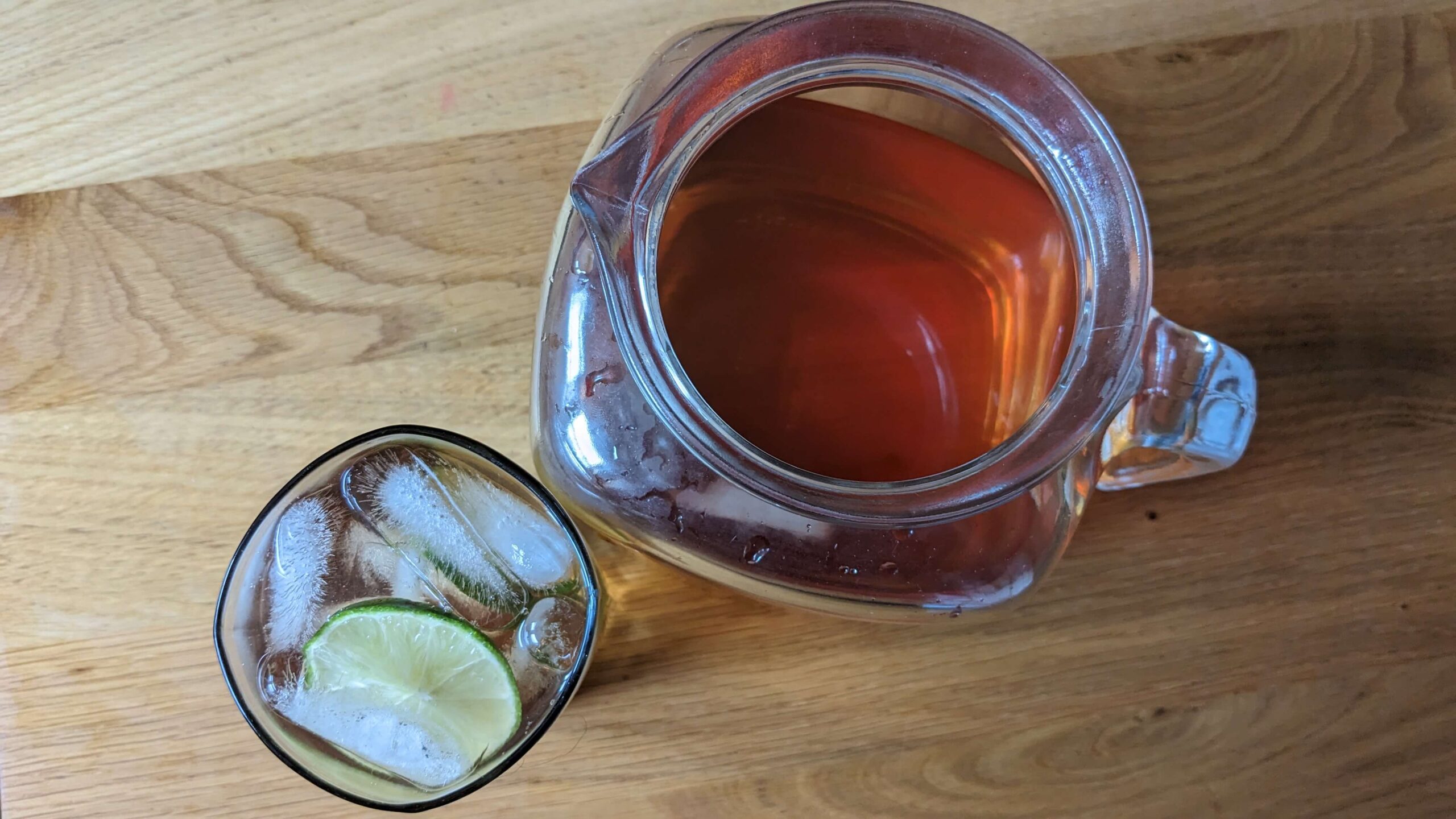 pitcher of basil tea next to a glass of tea with ice and a slice of lime