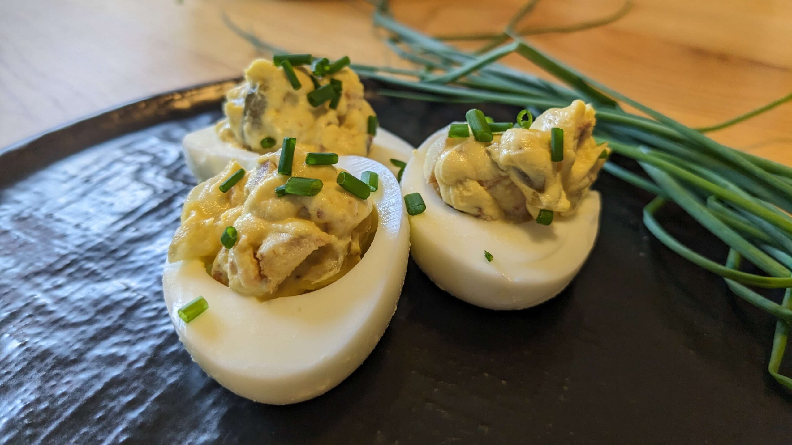 three savory bacon deviled eggs on a black plate topped with chopped chives