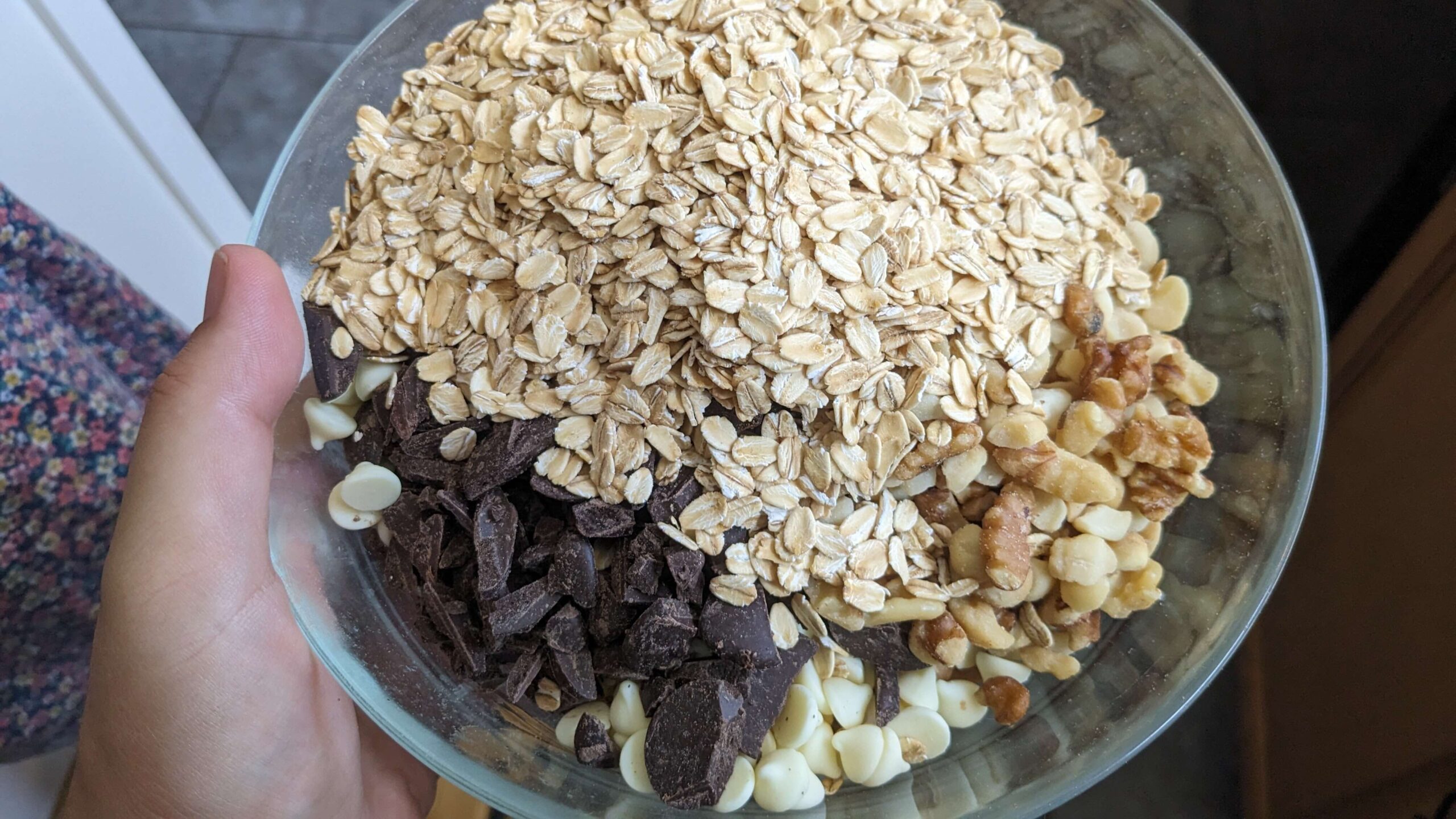 woman holding a bowl containing oats, chocolate chunks, walnuts, and white chocolate chips
