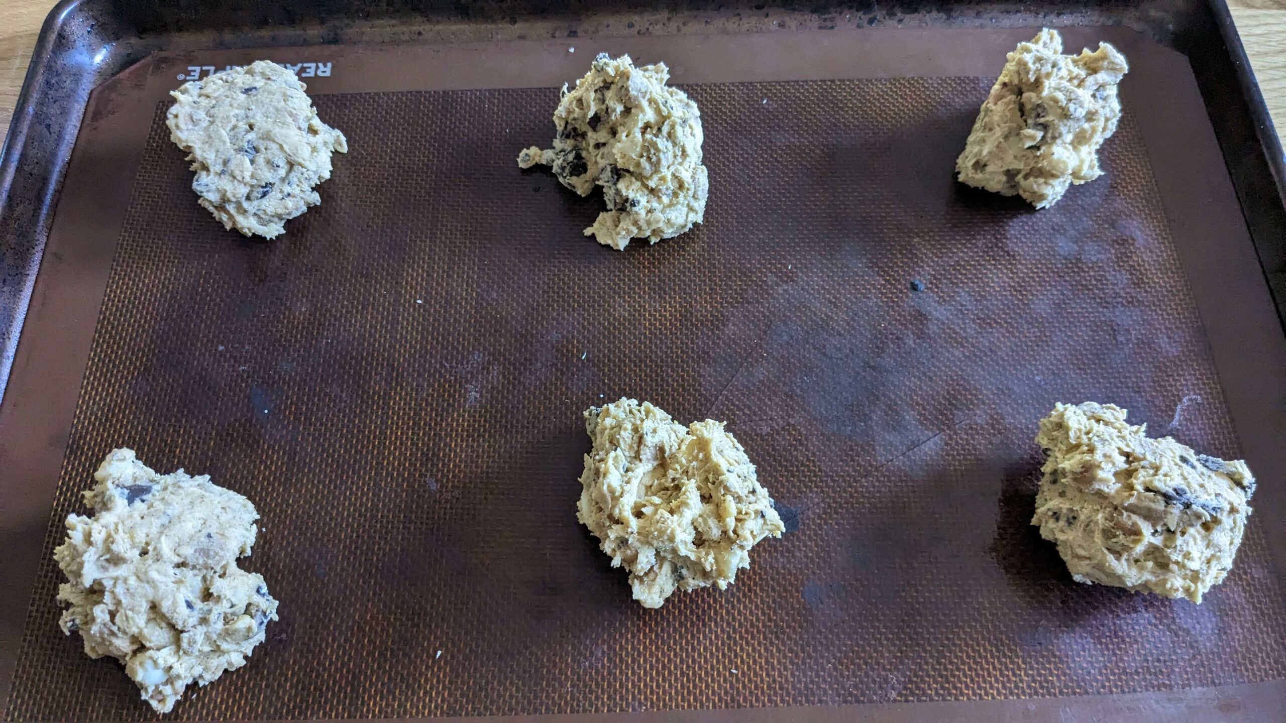 six mounds of raw cookie dough on a cookie sheet