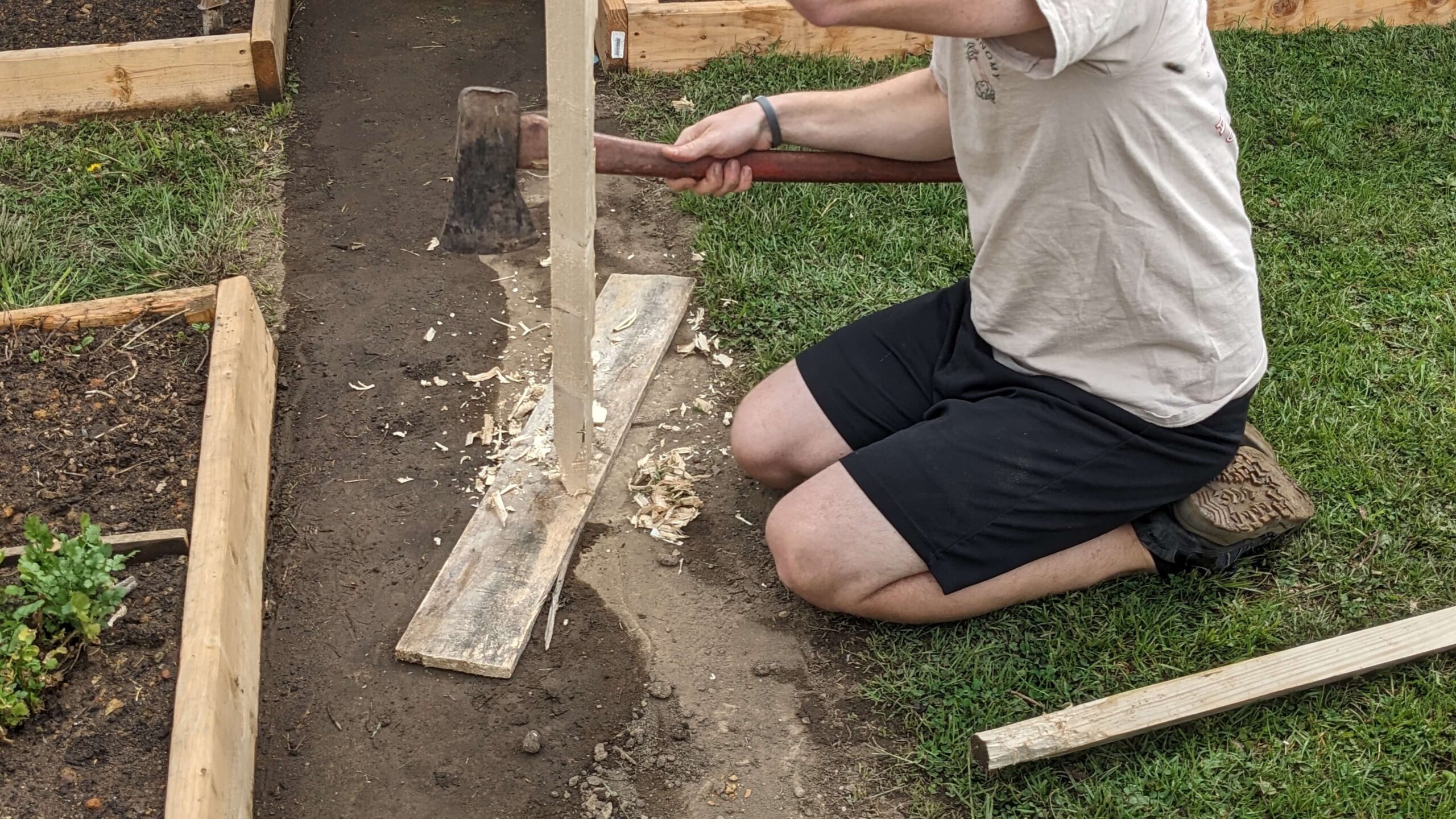 man using an ax to sharpen the bottom of a square piece of wood