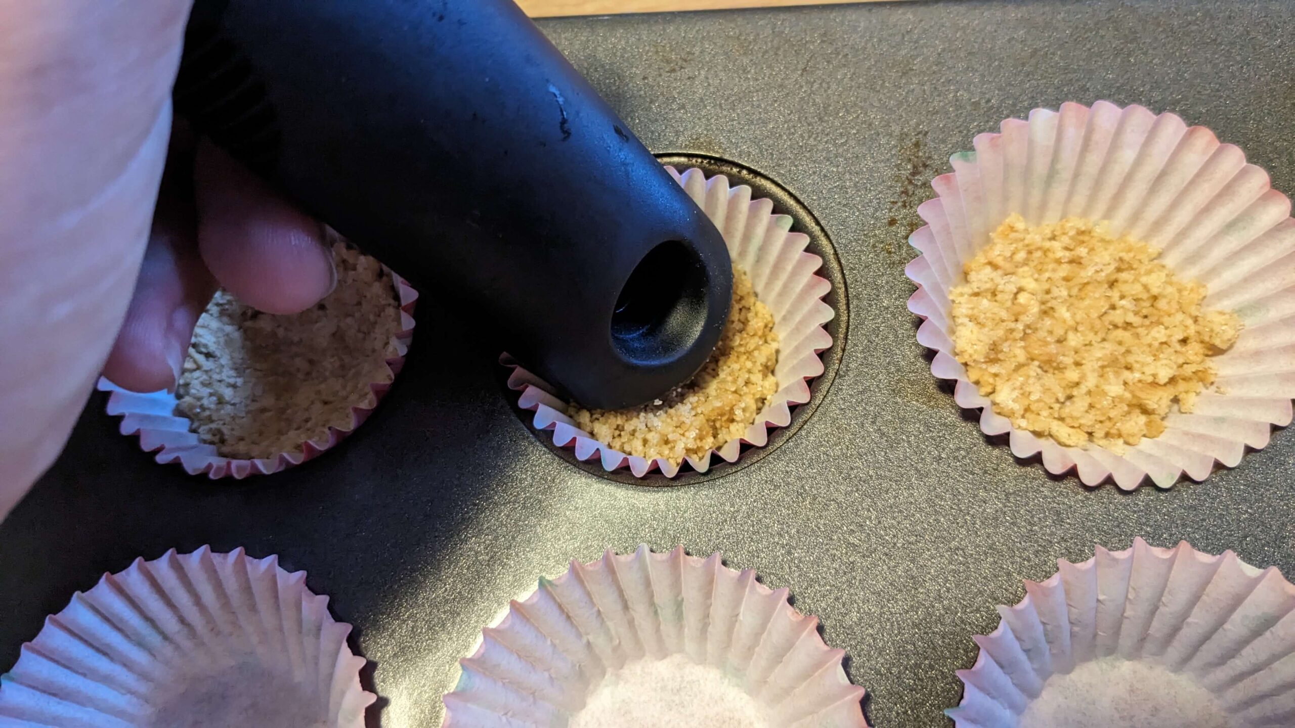 graham cracker crust being pressed into a mini muffin tin