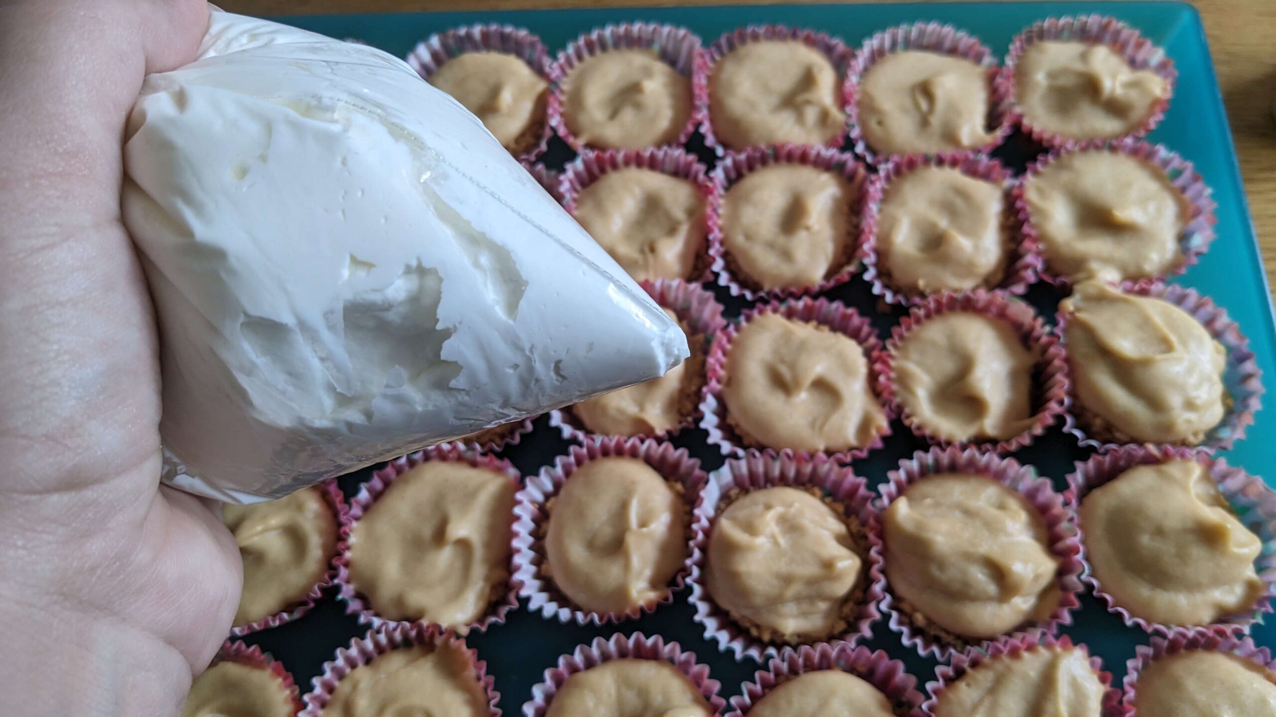 woman holding a bag of whipped cream over a tray of mini muffin peanut butter cheesecake bites