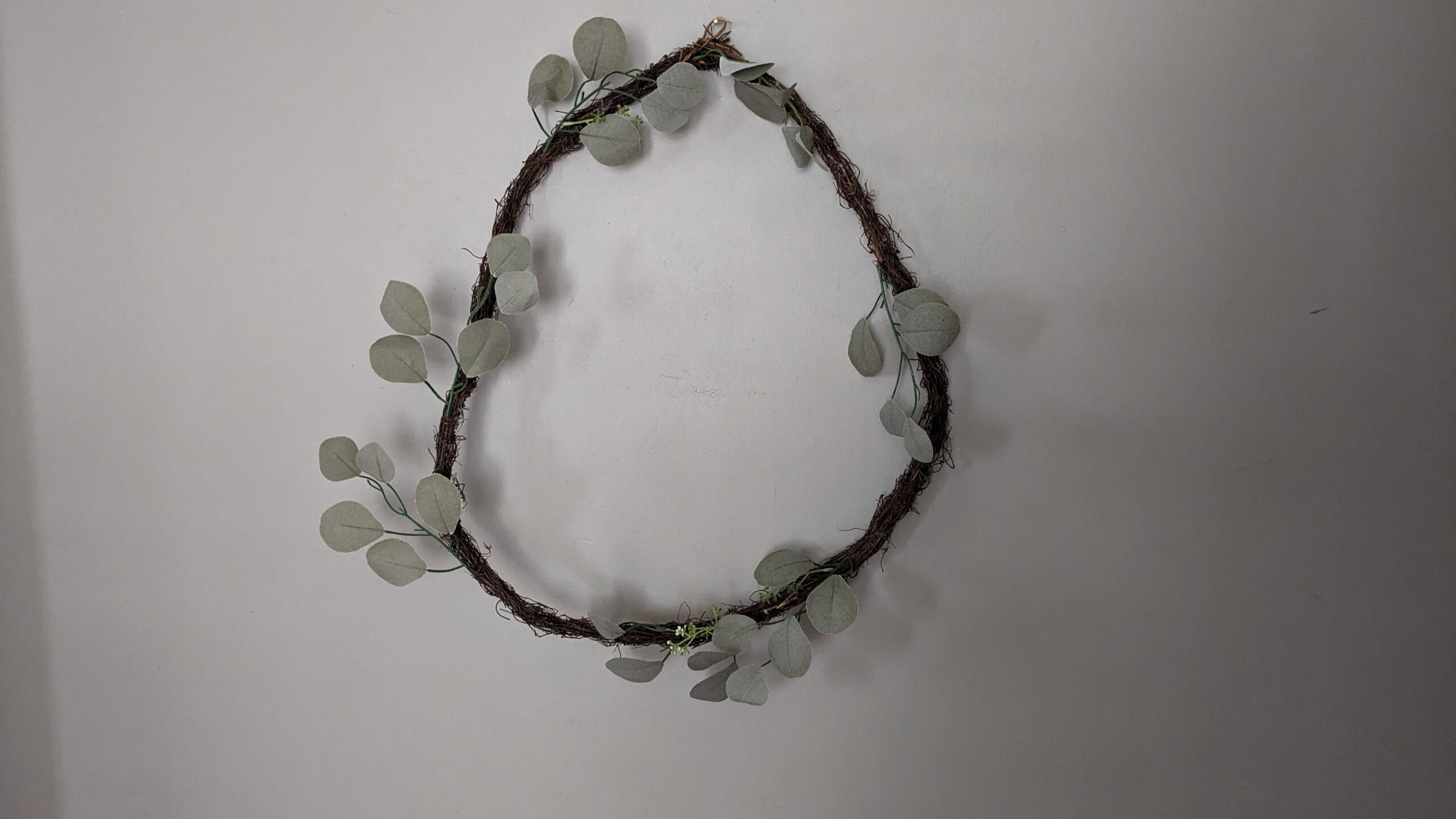 a fake grapevine wreath with scattered eucalyptus leaves hanging on a wall