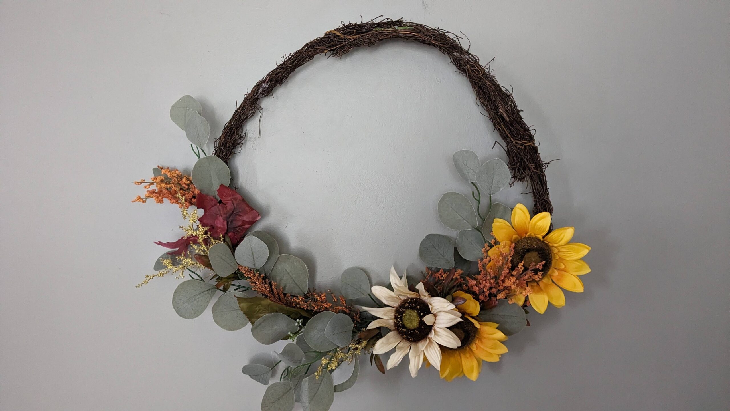 fall wreath with eucalyptus leaves, orange beads, two yellow sunflower heads and one cream sunflower head
