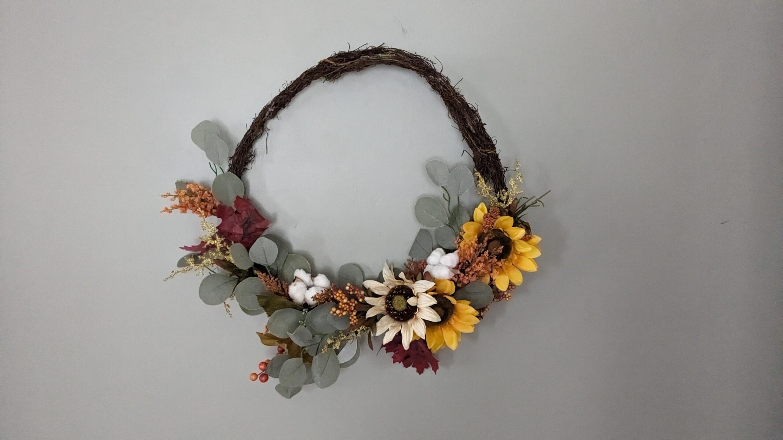 fall wreath with eucalyptus leaves, heads of cotton, orange beads, two yellow sunflower heads and one cream sunflower head