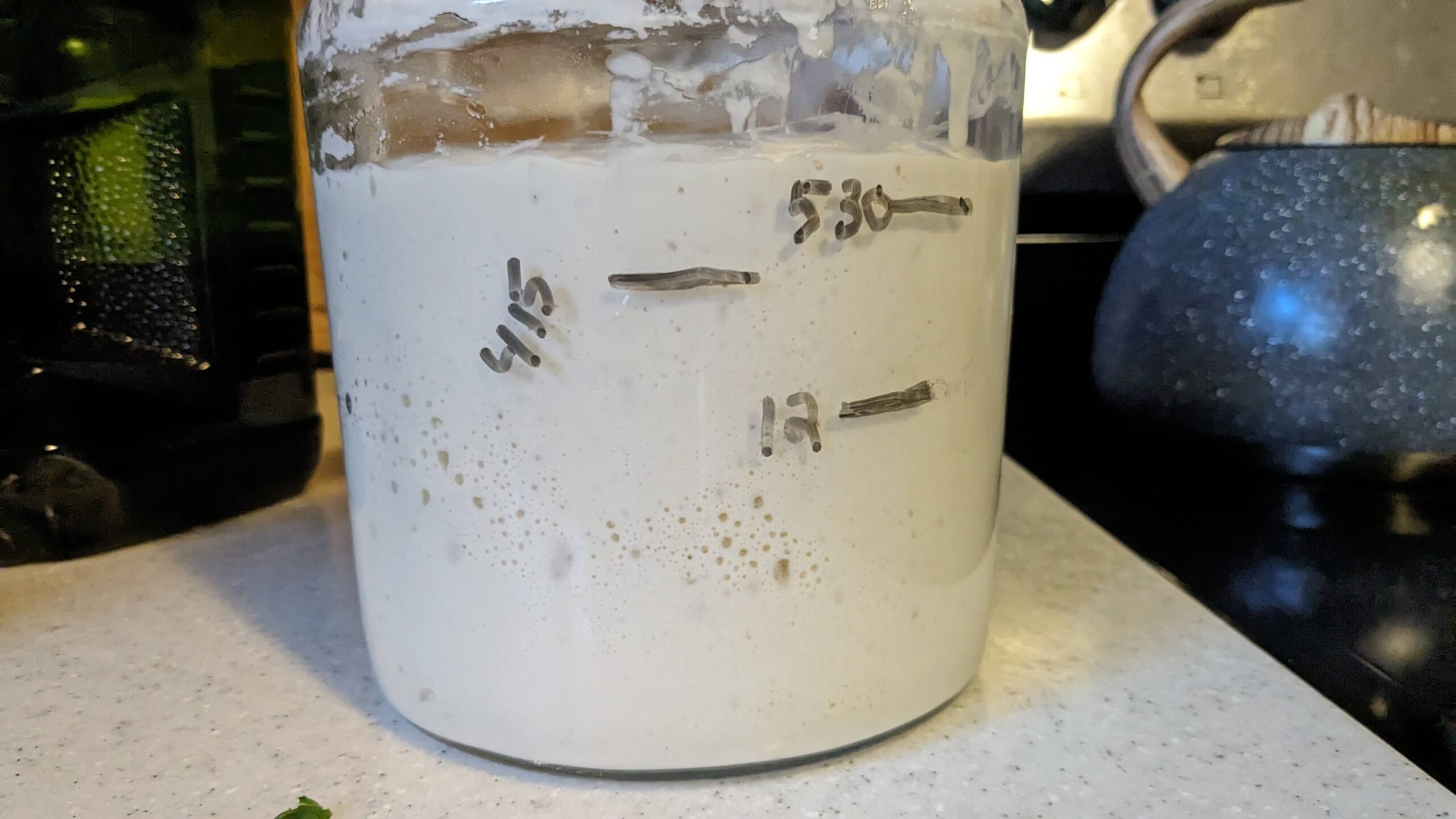 jar of rising sourdough starter on a stove top showing a span of 4 hours and then 5 and a half and higher