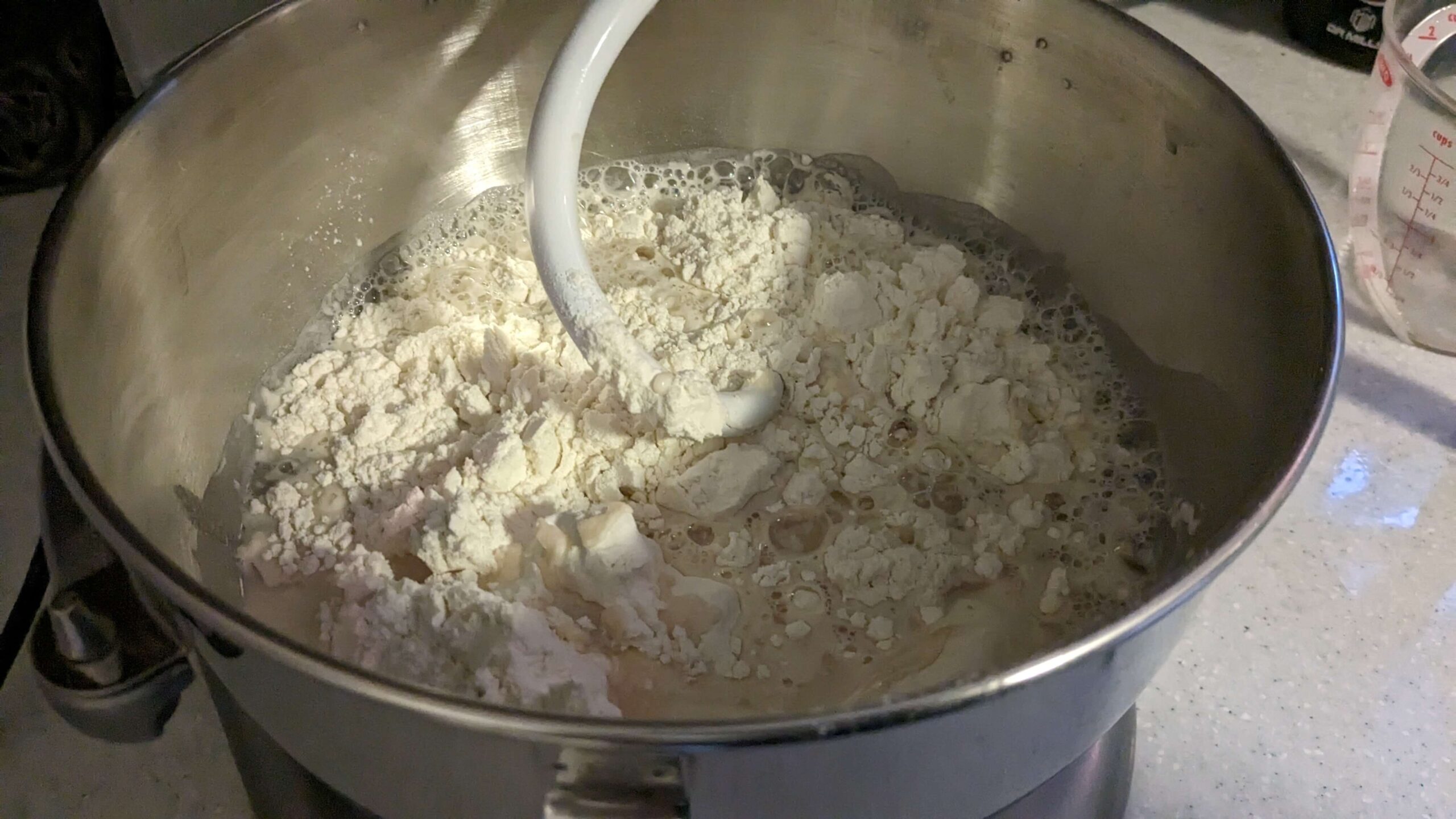 wet and dry ingredients in the bowl of a kitchen aid mixer with a dough hook