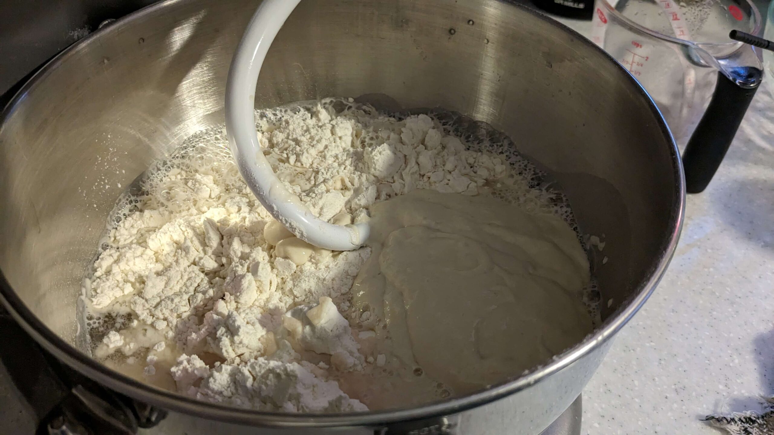 sourdough starter in a wet dough mixture in the bowl of a kitchen aid mixer with a dough hook