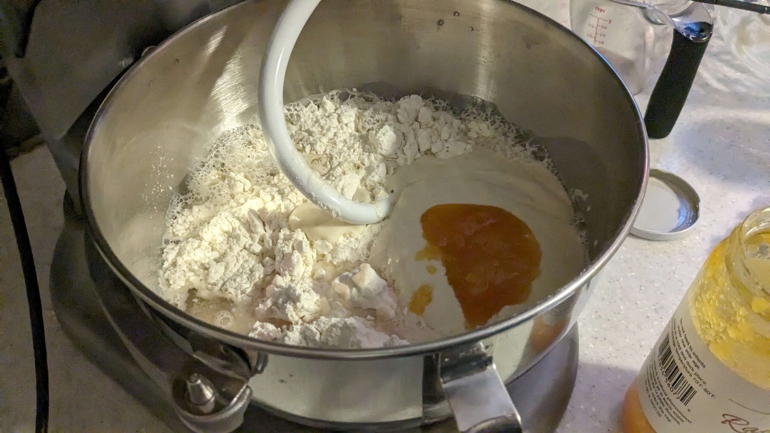 honey and sourdough starter in a wet dough mixture in the bowl of a kitchen aid mixer with a dough hook