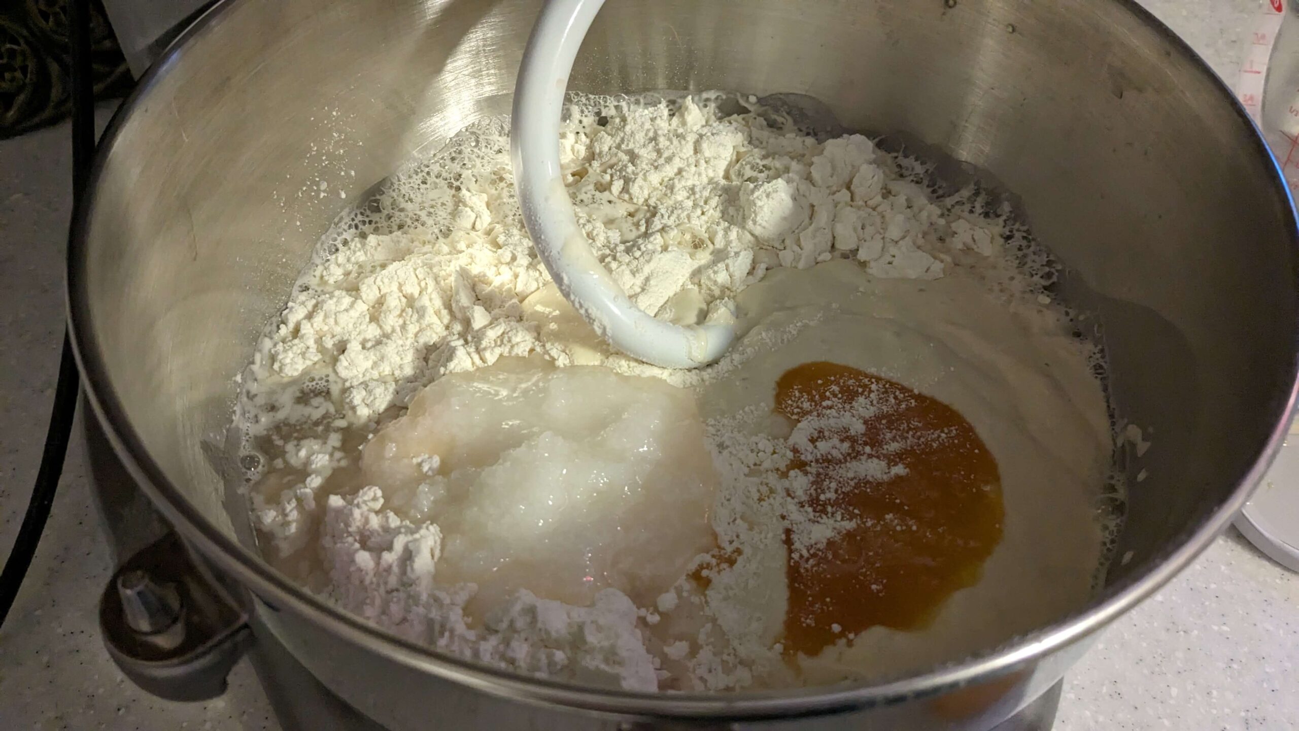 coconut oil, honey and sourdough starter in a wet dough mixture in the bowl of a kitchen aid mixer with a dough hook