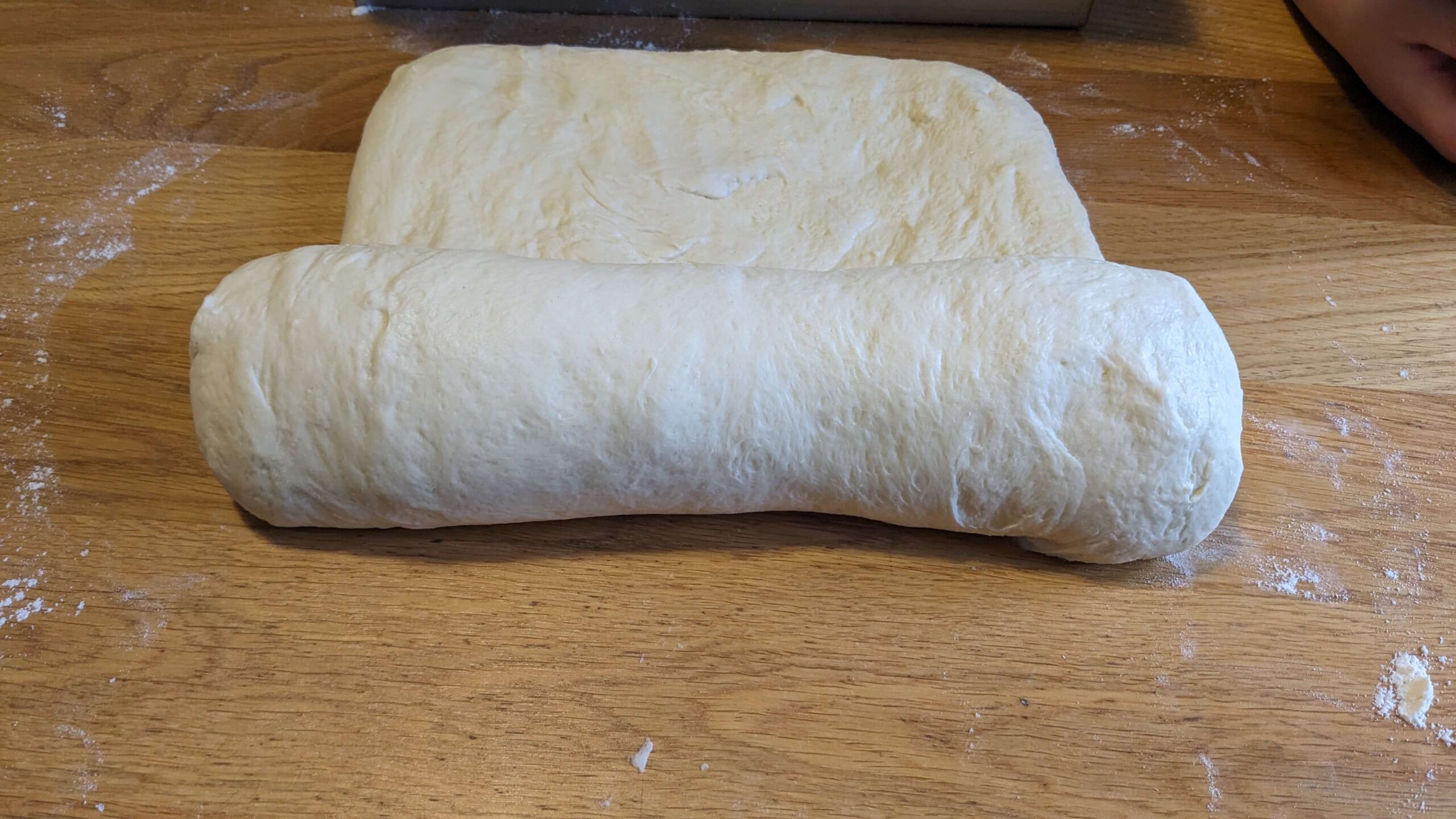 rectangle of bread dough half rolled on a wooden surface