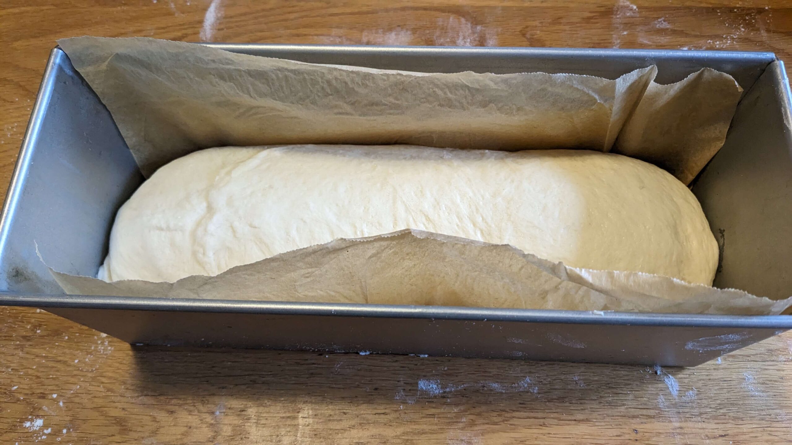 bread dough in a pullman loaf pan with parchment paper