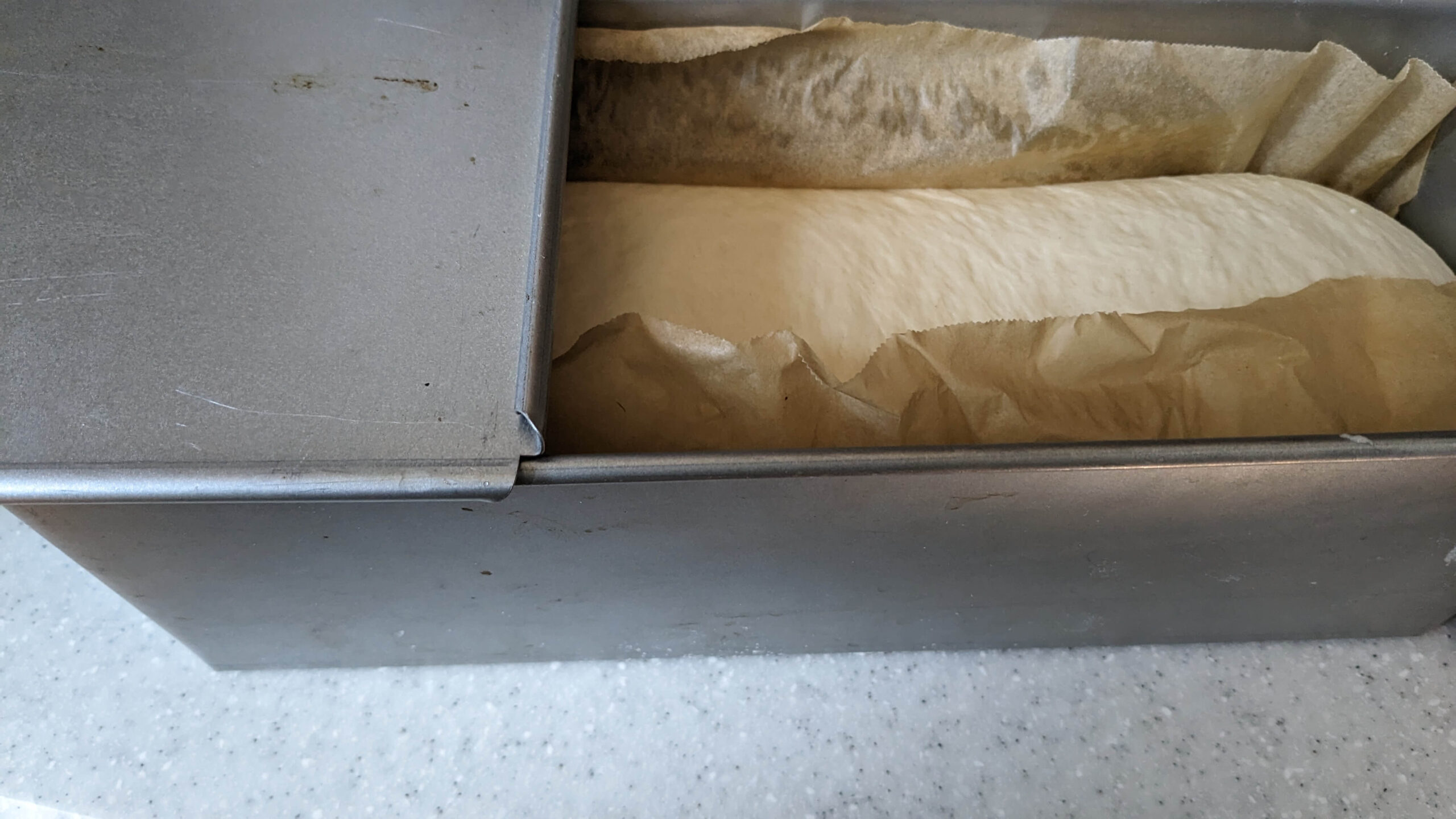 loaf of bread dough in a pullman loaf pan with the lid halfway pulled back