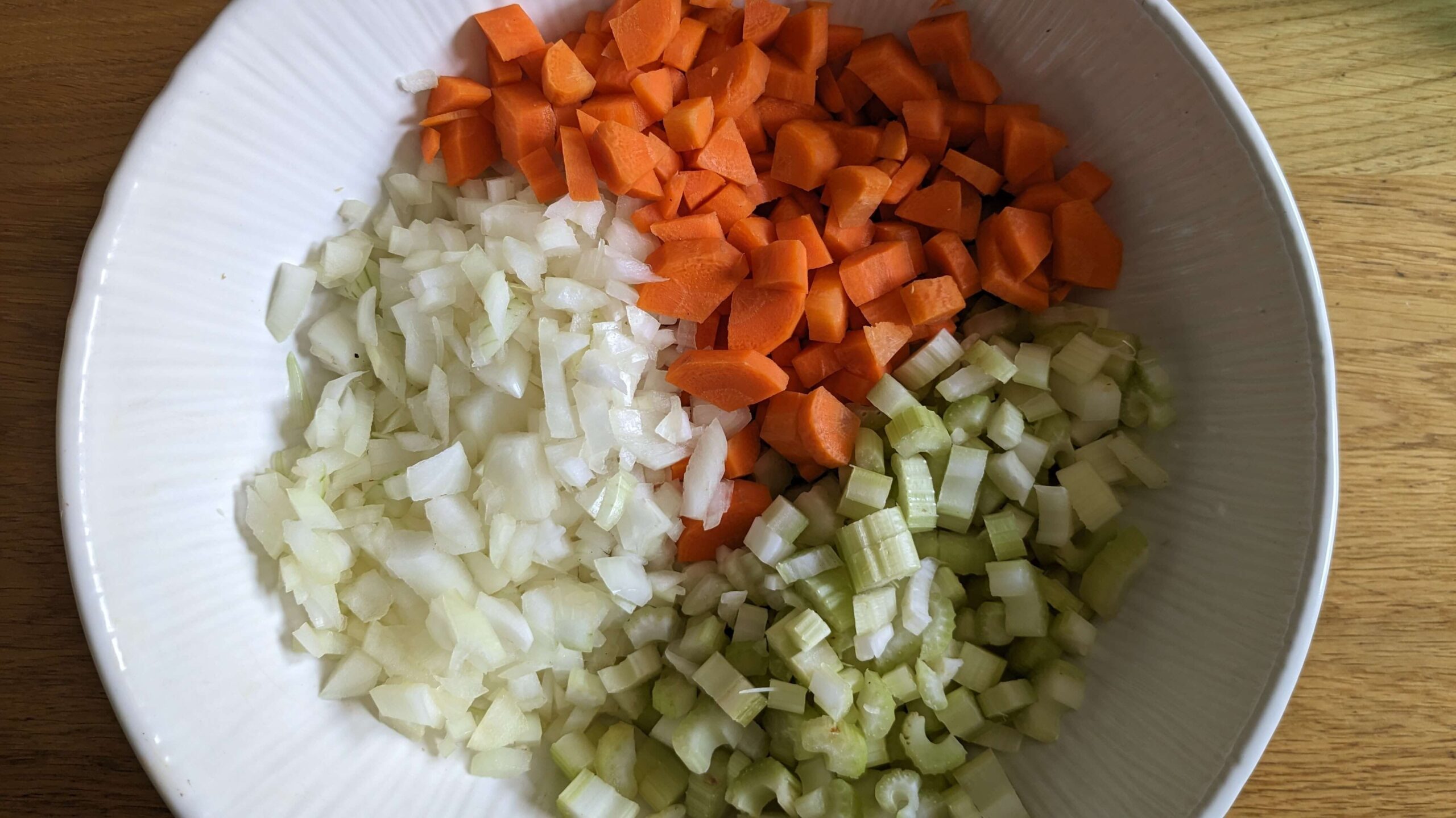 white bowl filled with equal amounts of diced carrots, diced cellery, and diced onions