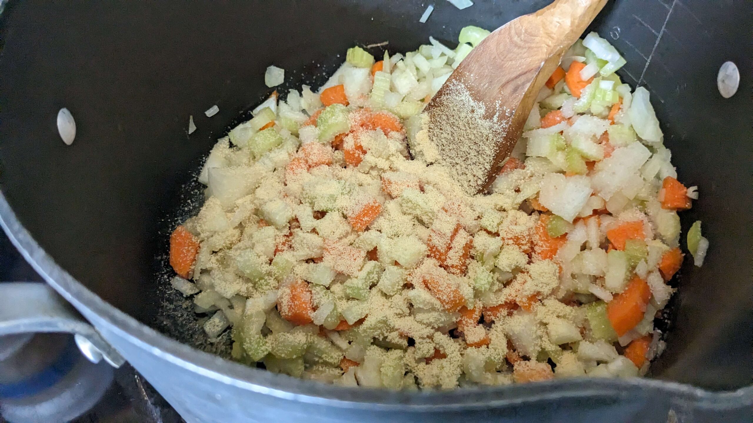 diced vegetables sauteing in a pot with a wooden spatula
