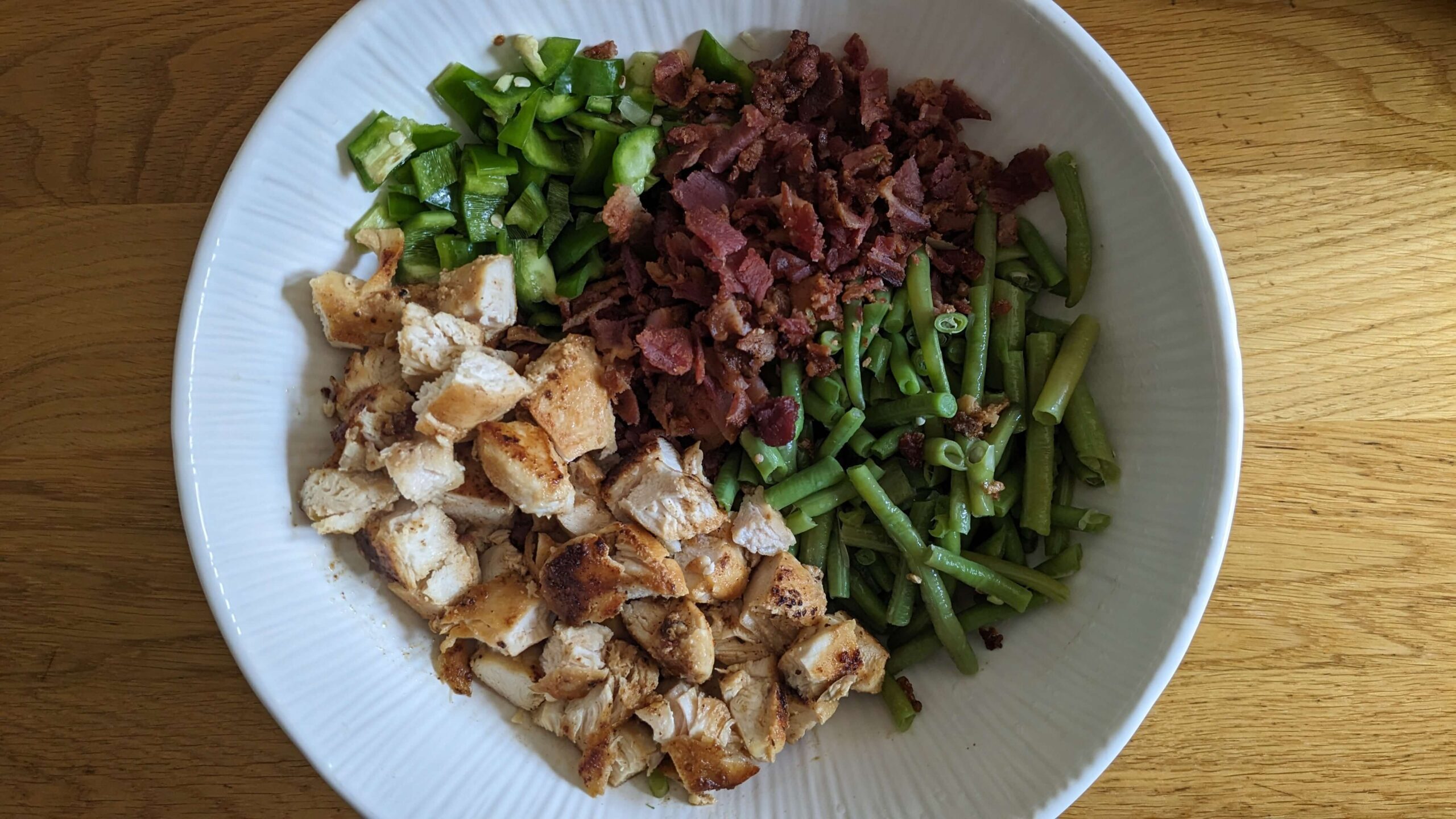 a white bowl filled with chopped cooked chicken, diced peppers, diced cooked bacon, and chopped green beans