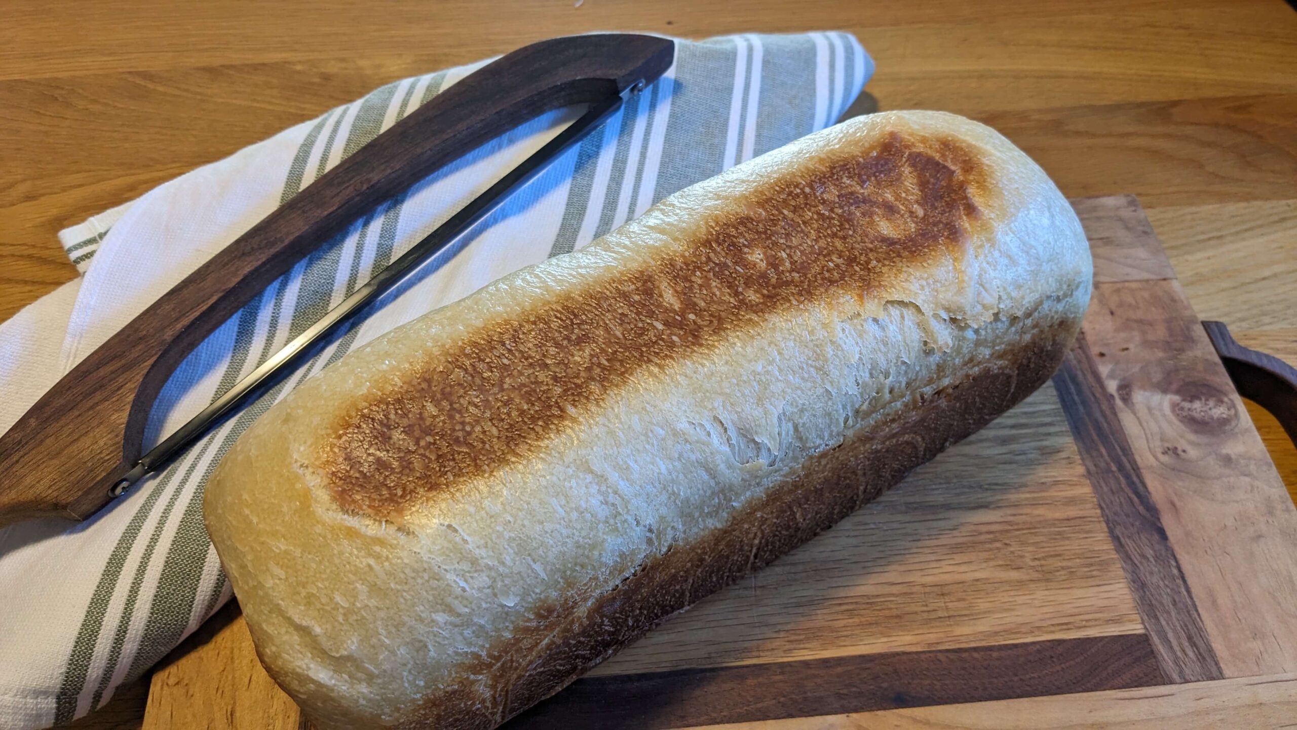 pullman shaped sandwich loaf on a wooden cutting board next to a bow knife on a towel
