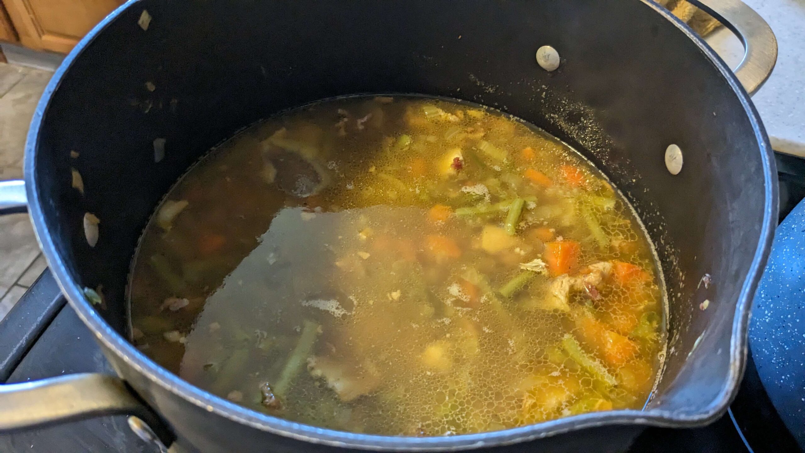 a pot filled with stock and chopped vegetables and chicken