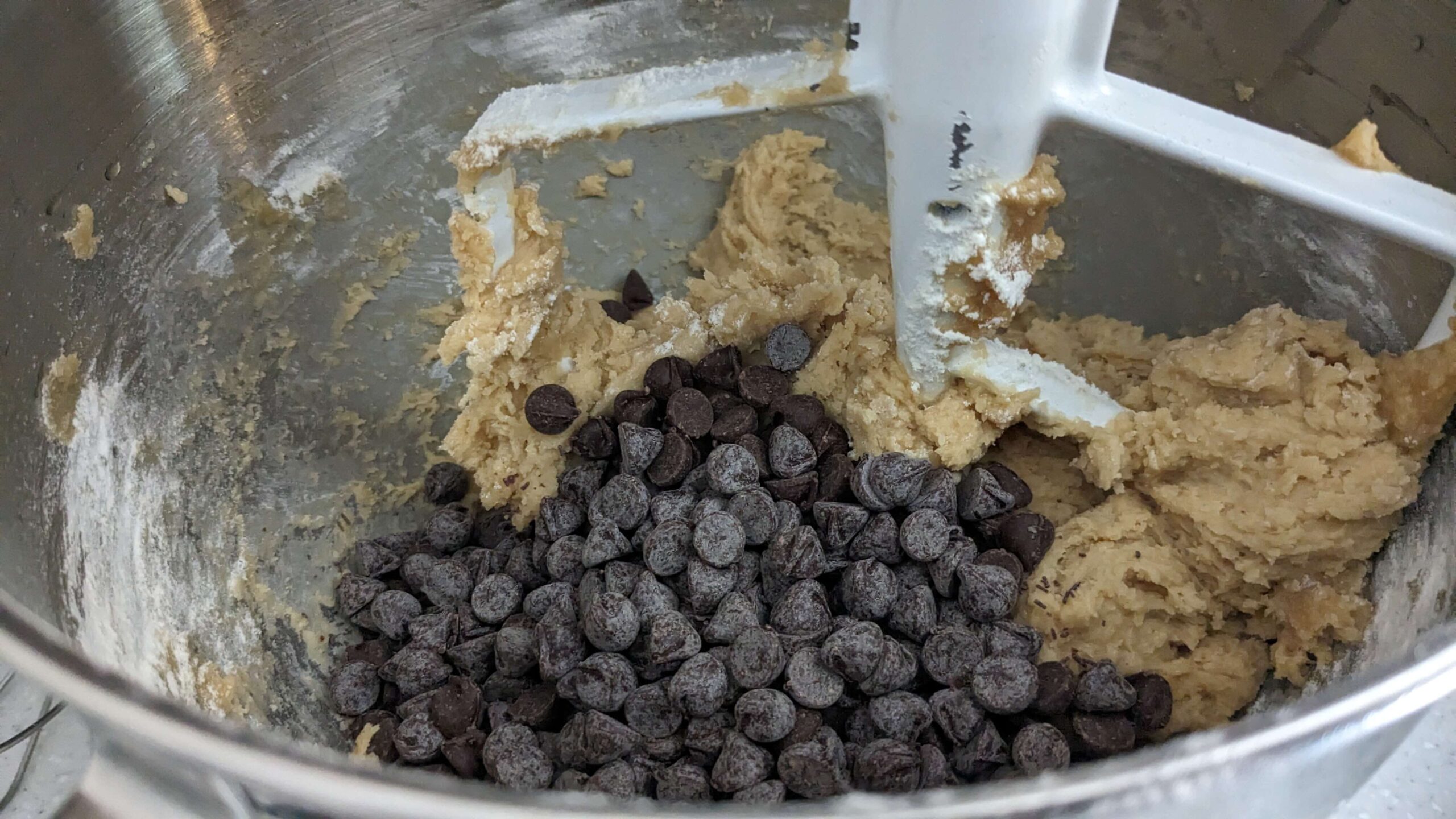 chocolate chips on top of dough in a kitchen aid mixer with a beater attachment