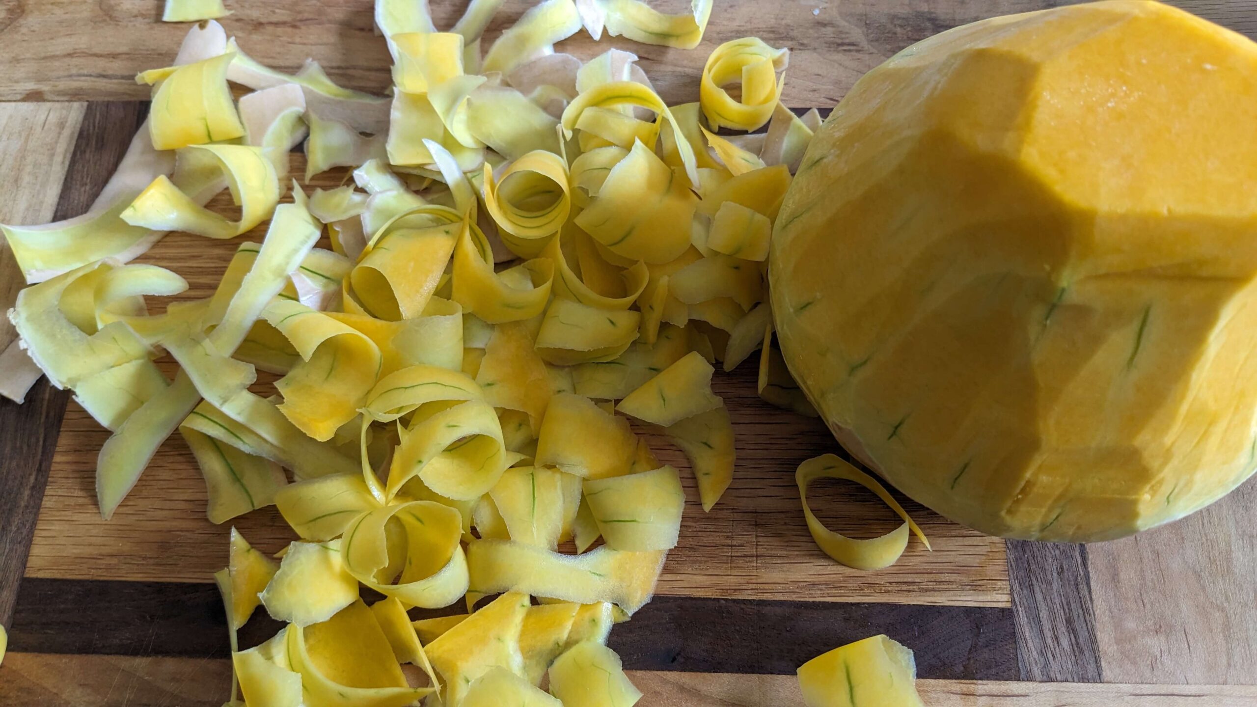 peeled butternut squash next to curled peeled rinds on a cutting board